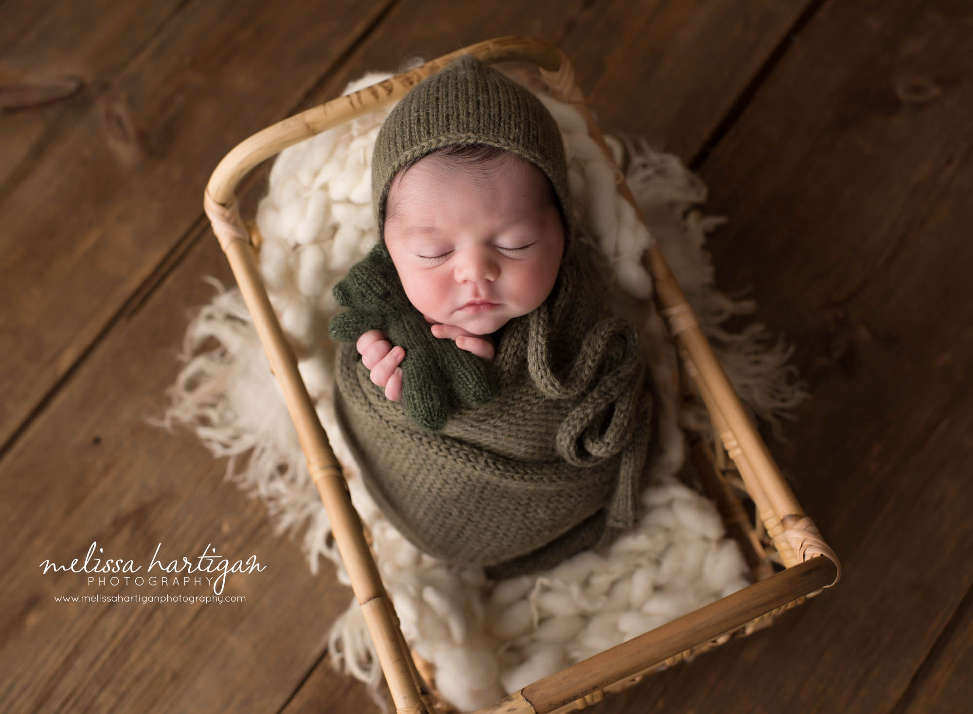 Newborn baby boy posed in a basket wrapped in green knitted wrap holding green teddy Newborn Photography Ellington CT
