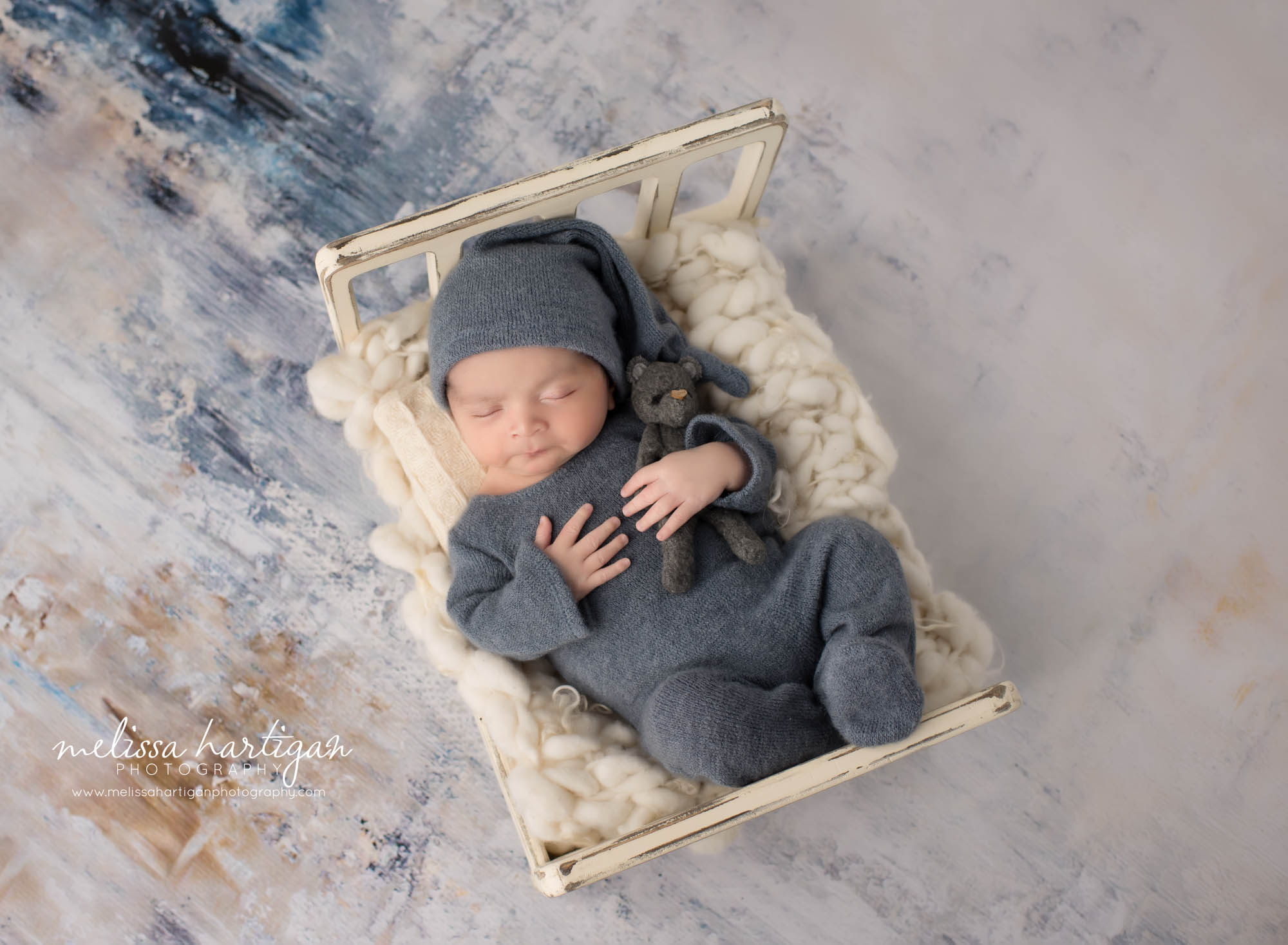 Newborn baby boy posed on wooden cream bed holding teddy