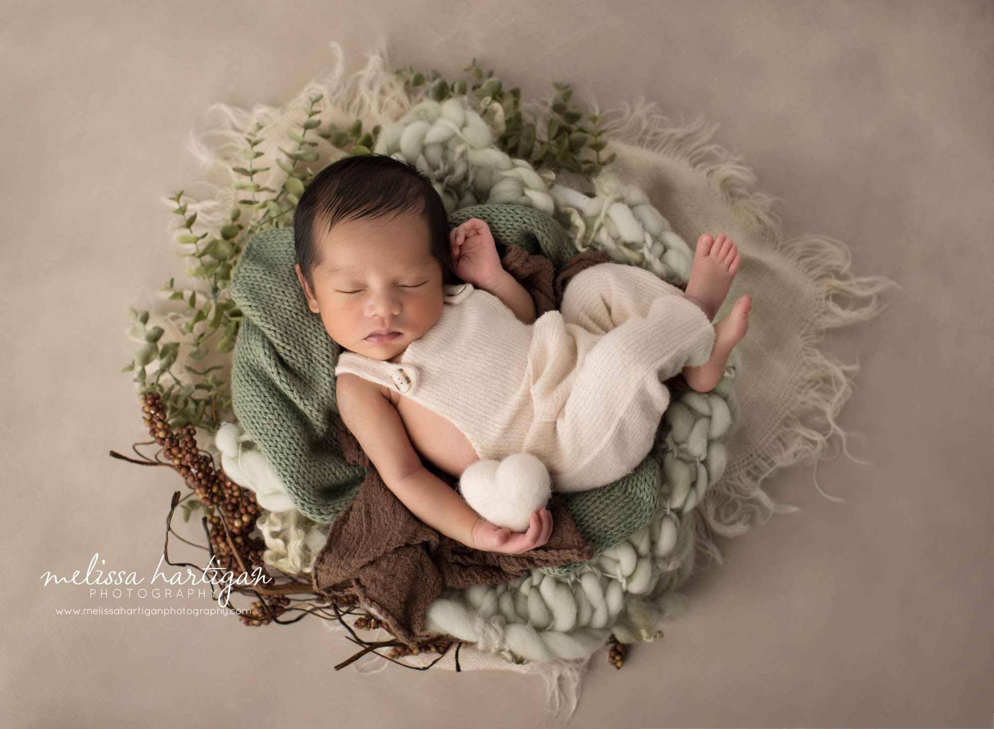 Newborn baby boy posed wearing cream outfit posed in green and cream colors and props