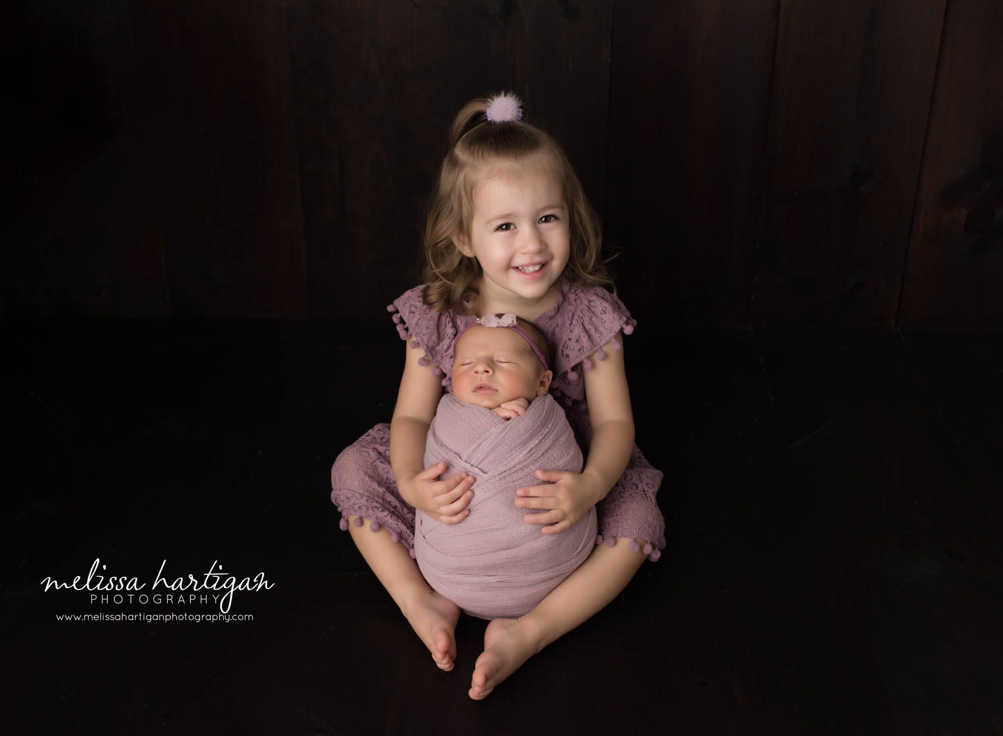 big sister sitting smiling happy with newborn baby sister