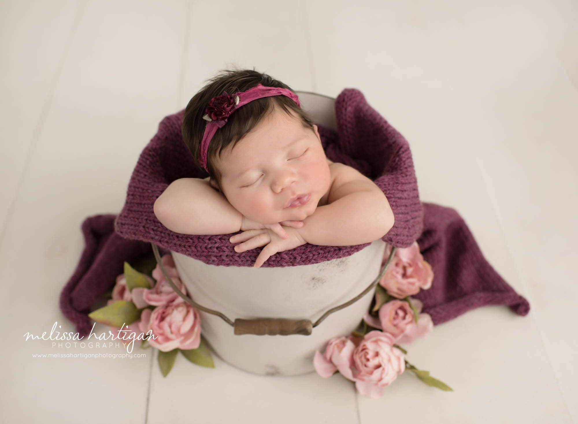 newborn baby girl posed in bucket sleeping peacefully with flowers around Newborn Photography Farmington CT