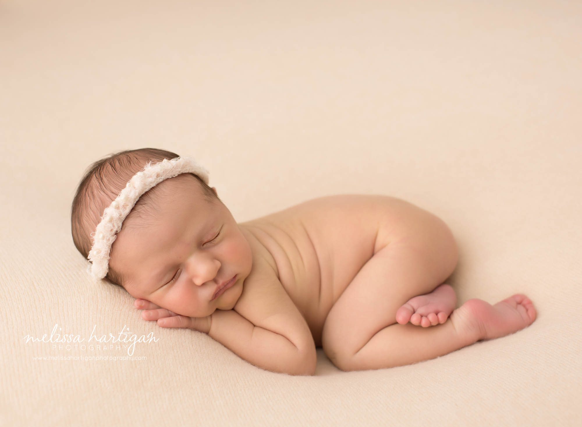newborn baby girl posed on tummy wearing cream headband