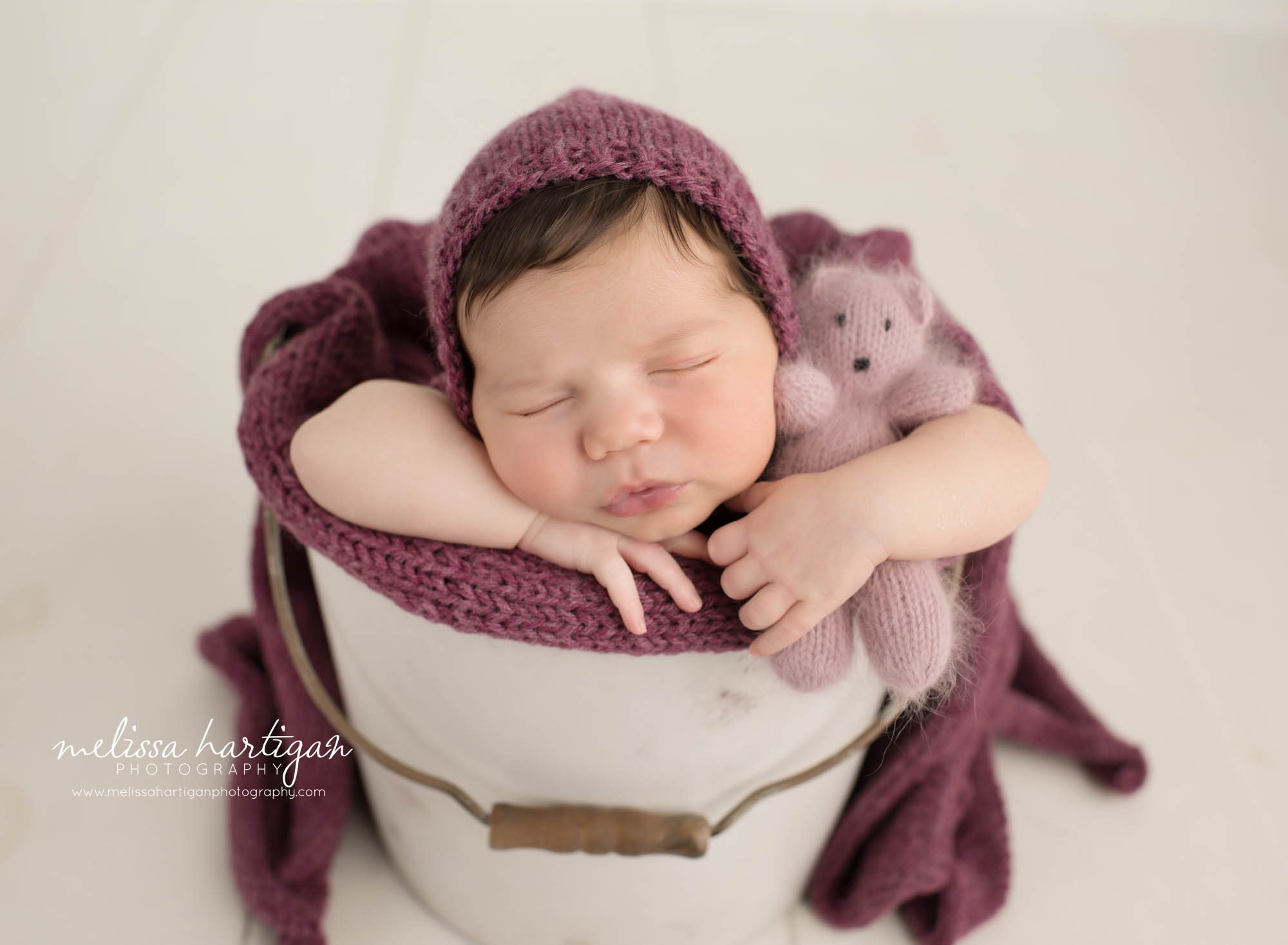 Newborn baby girl posed in bucket cuddling knitted newborn teddy bear