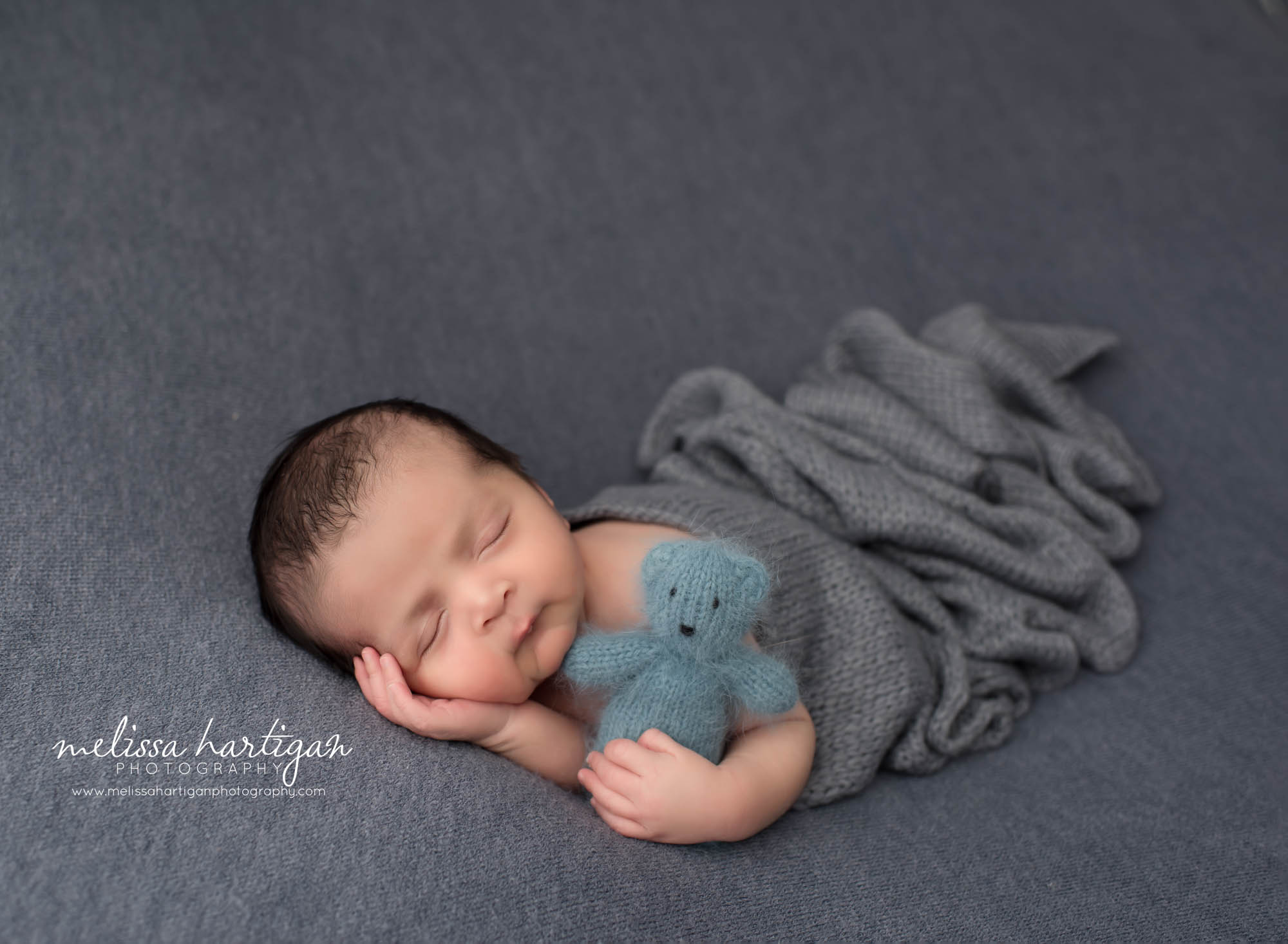 newborn baby boy posed on blue backdrop holding knitted teddy bear Manchester CT Newborn Photography