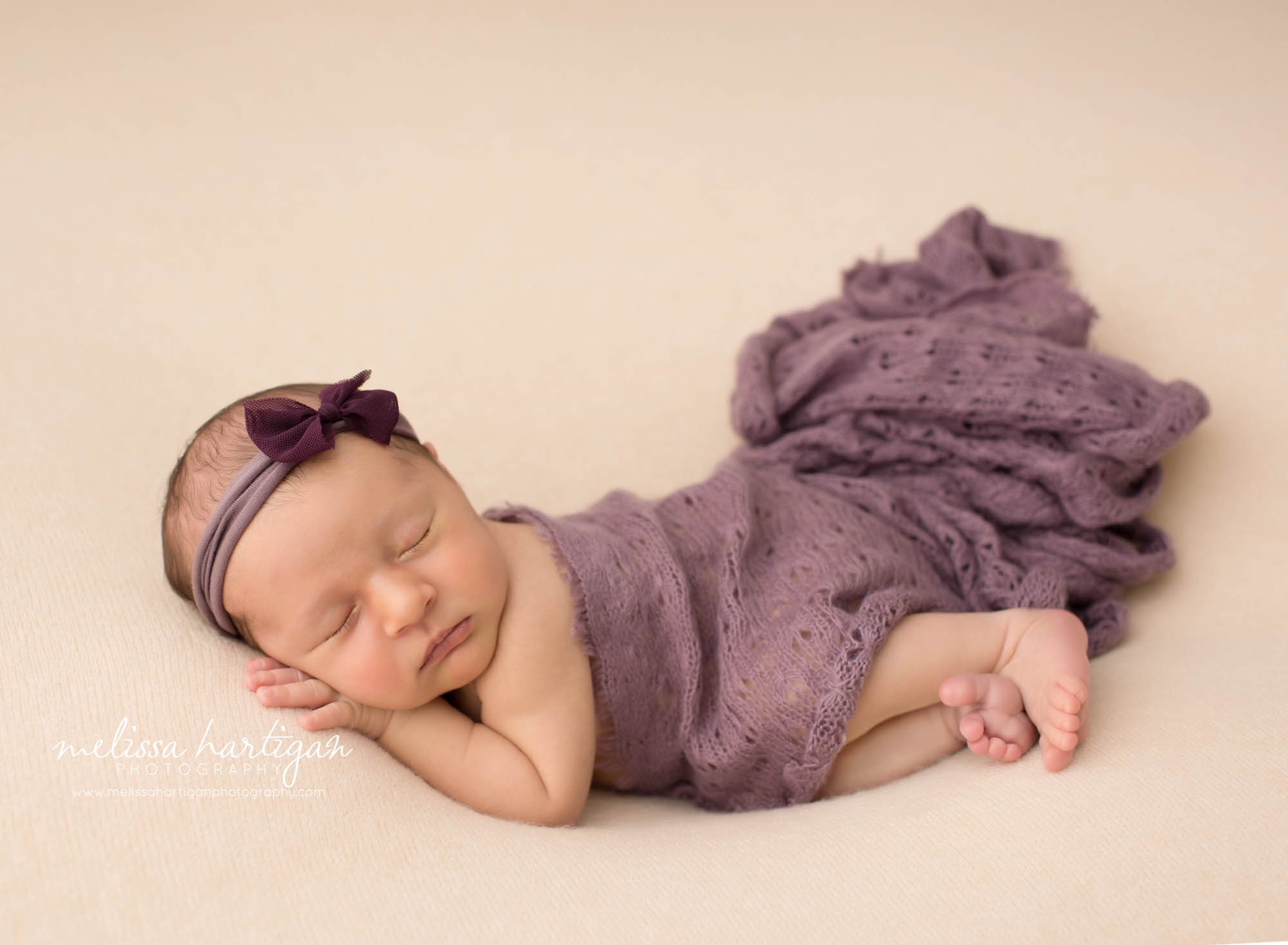 newborn baby girl pose don side with purple wrap draped over wearing bow headband Newborn Photography Weston CT