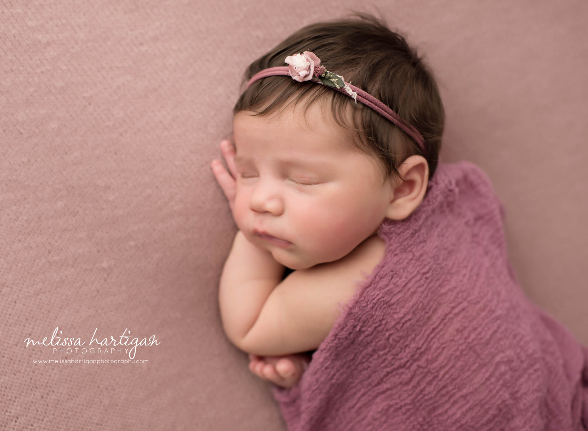 Newborn baby girl posed on tummy wearing flower headband Newborn Photography Farmington CT