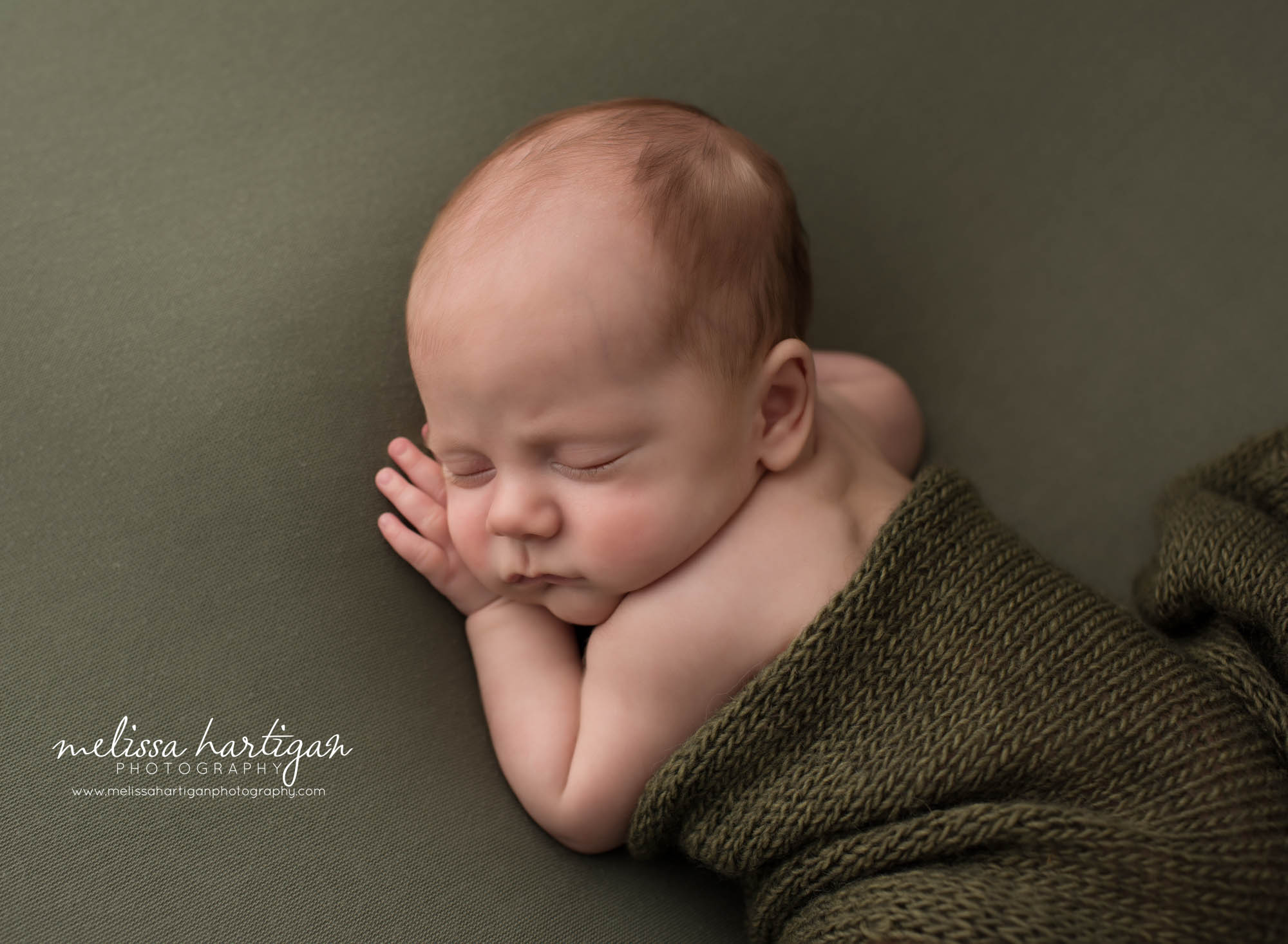 Newborn baby boy posed on side with green knitted layer