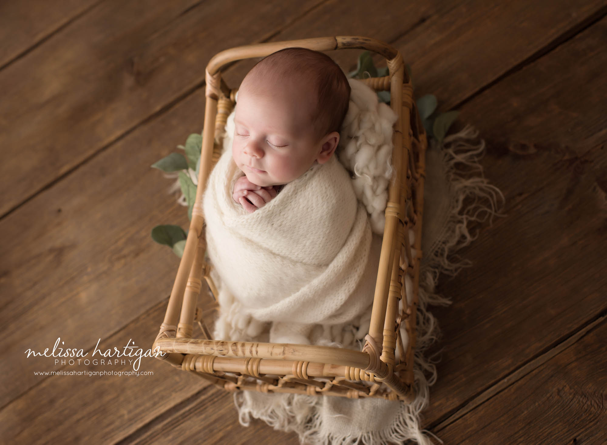 Newborn baby boy swaddled in knitted cream wrap posed in basket