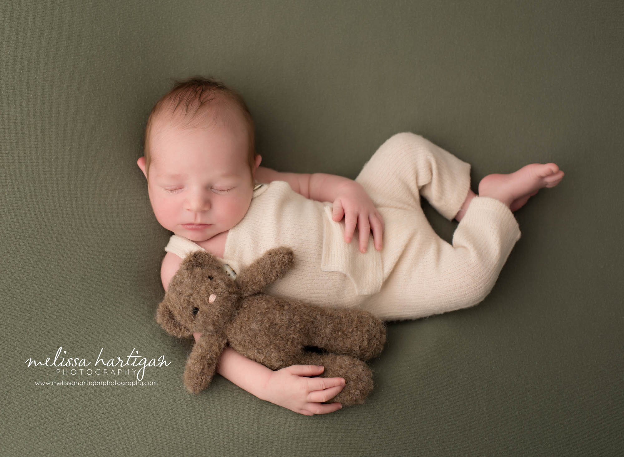 newborn baby boy posed on green backdrop wearing cream newborn outfit holding teddy bear Newborn Photography Portland CT