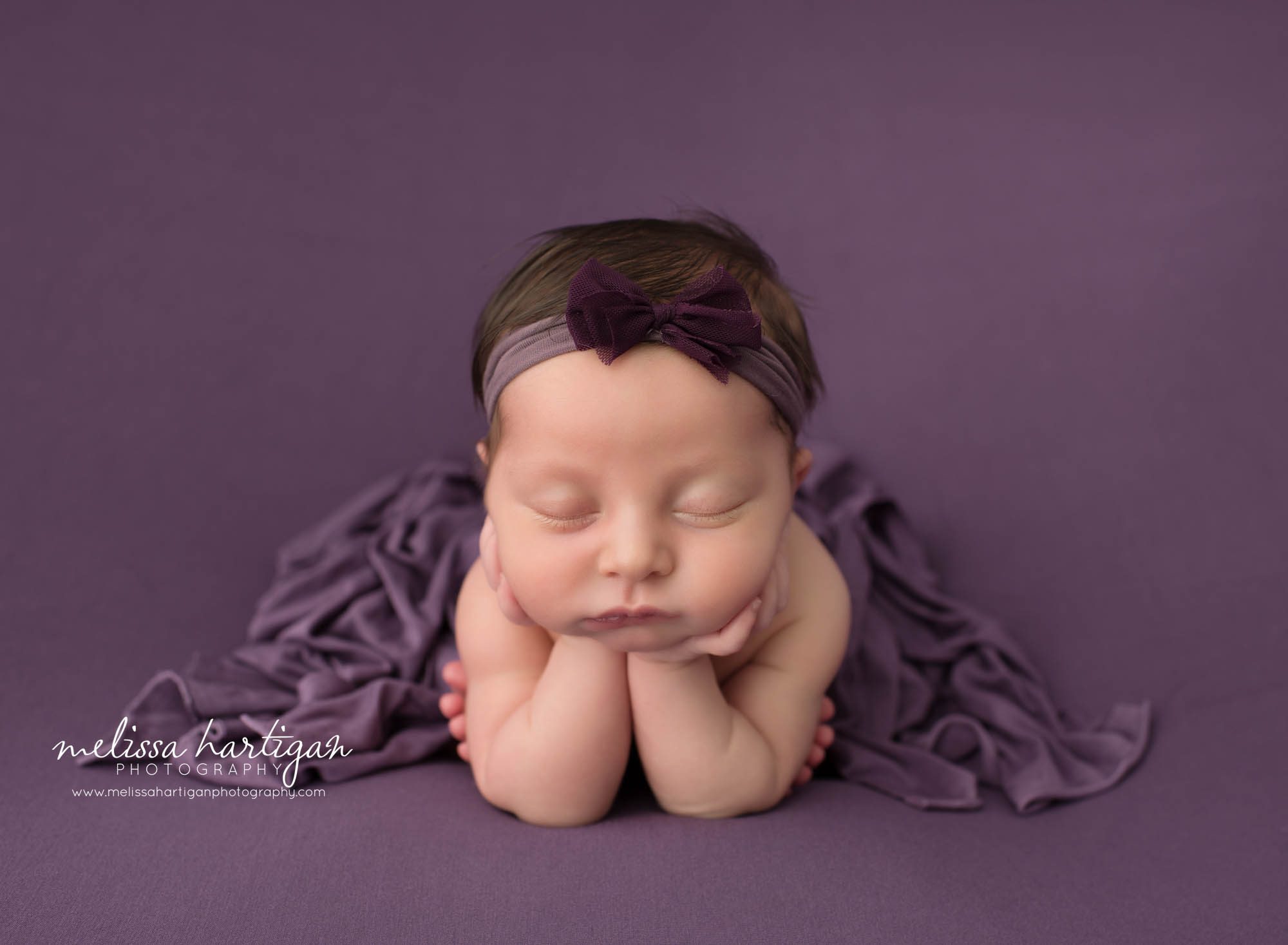 Newborn baby girl posed froggy pose wearing purple bow headband