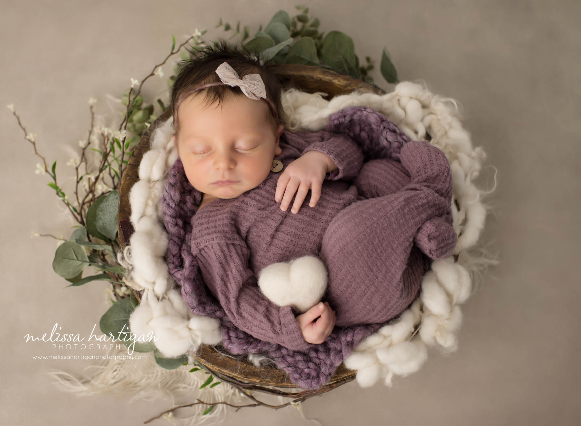 Newborn baby girl posed on wooden bowl weairng purple footed sleeper holding cream white felted heart prop Vernon CT Newborn Photography