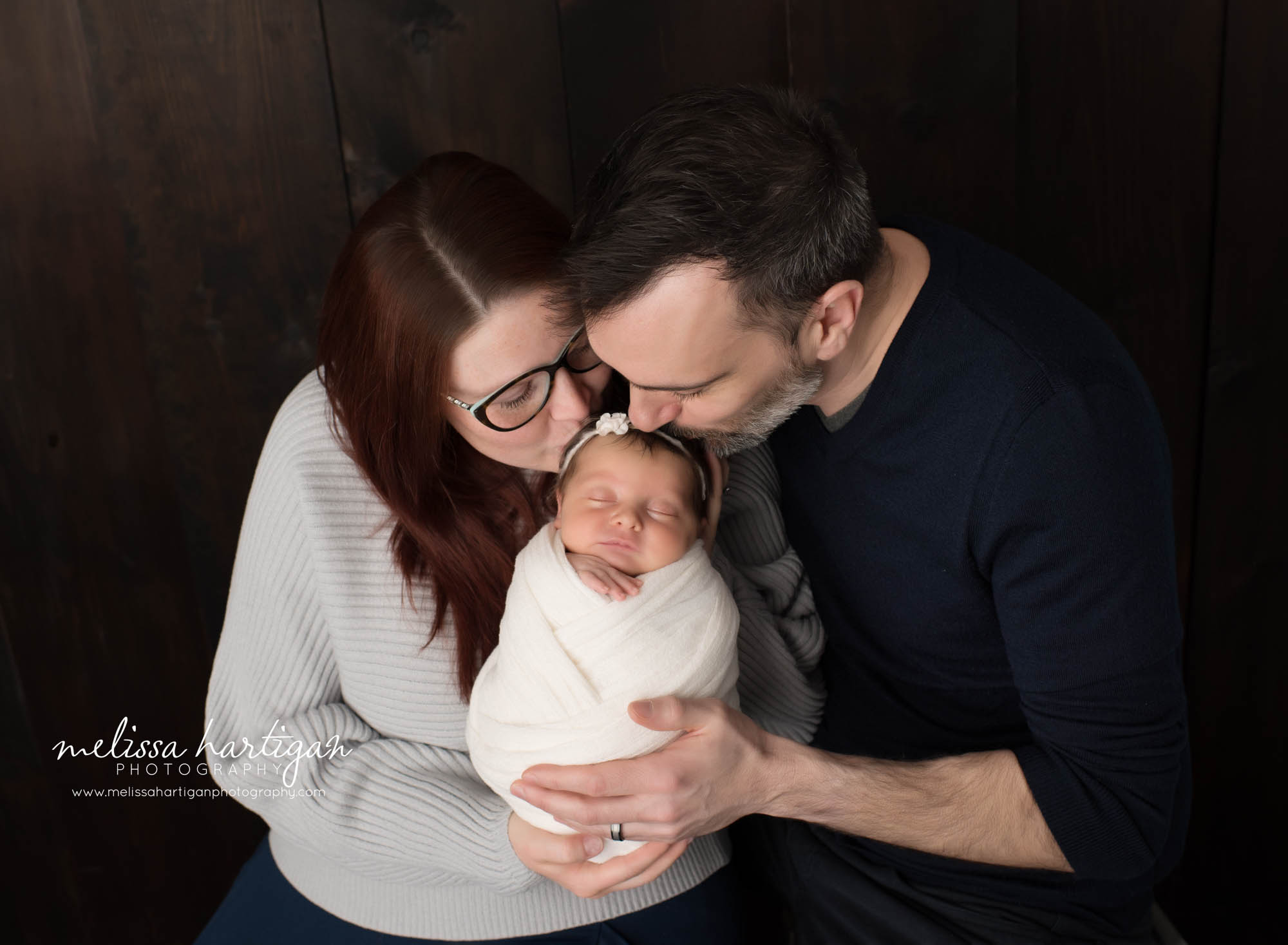 Mom dad kissing newborn daughter on head in family pose