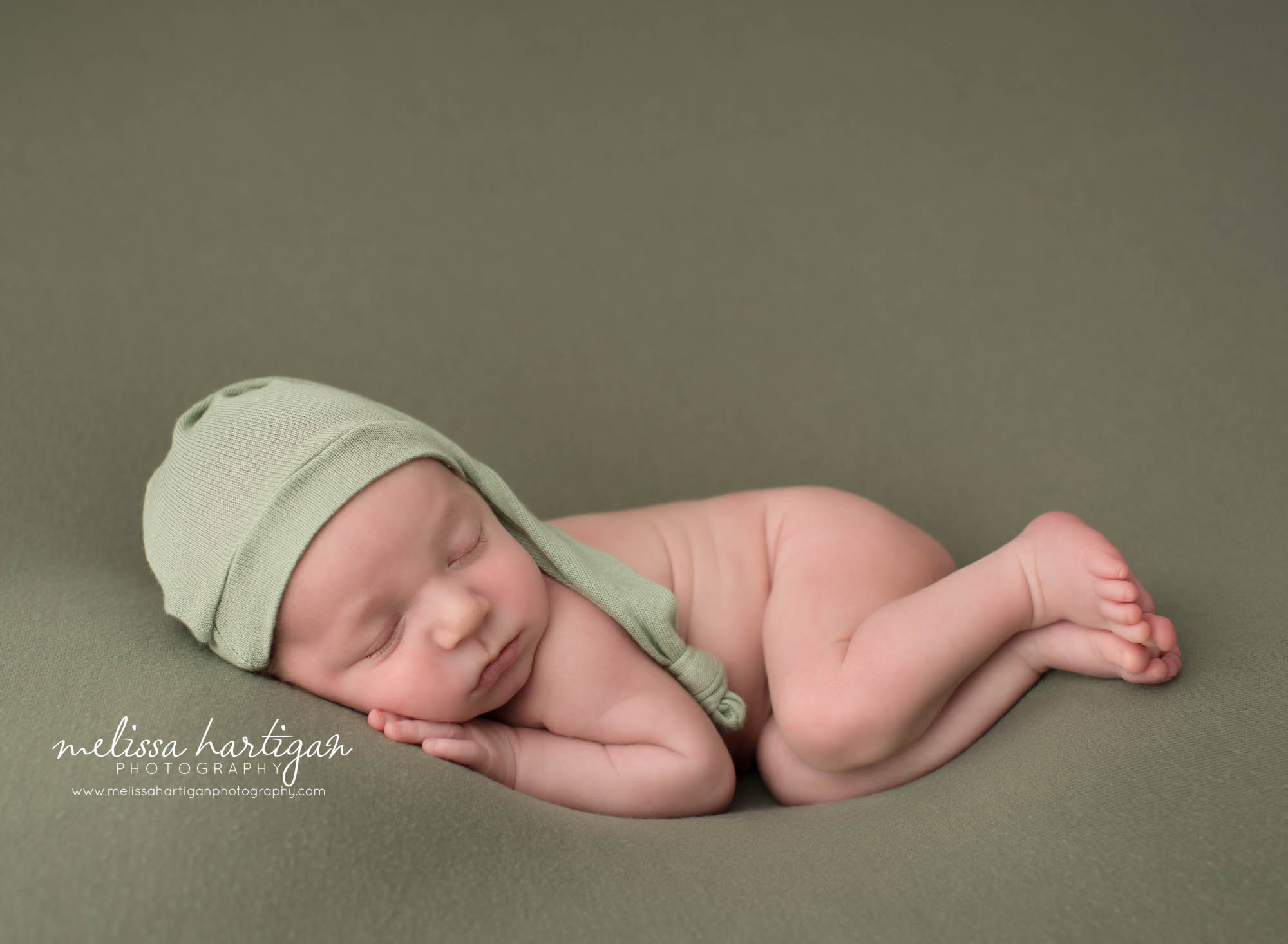 newborn baby boy posed on side wearing green sleepy cap Newborn Photography Portland CT