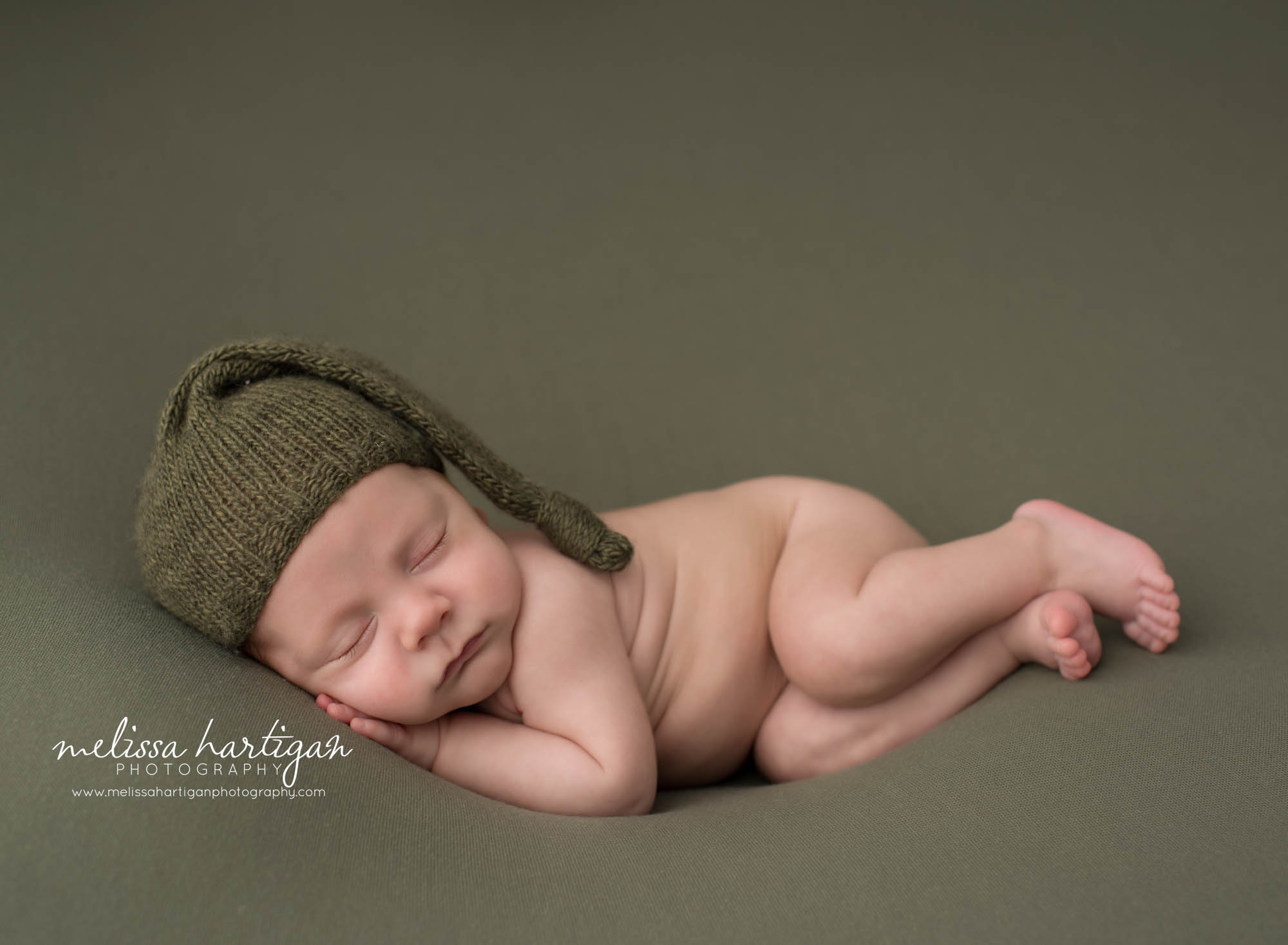 Newborn baby boy posed o0n side wearing knitted green sleepy cap