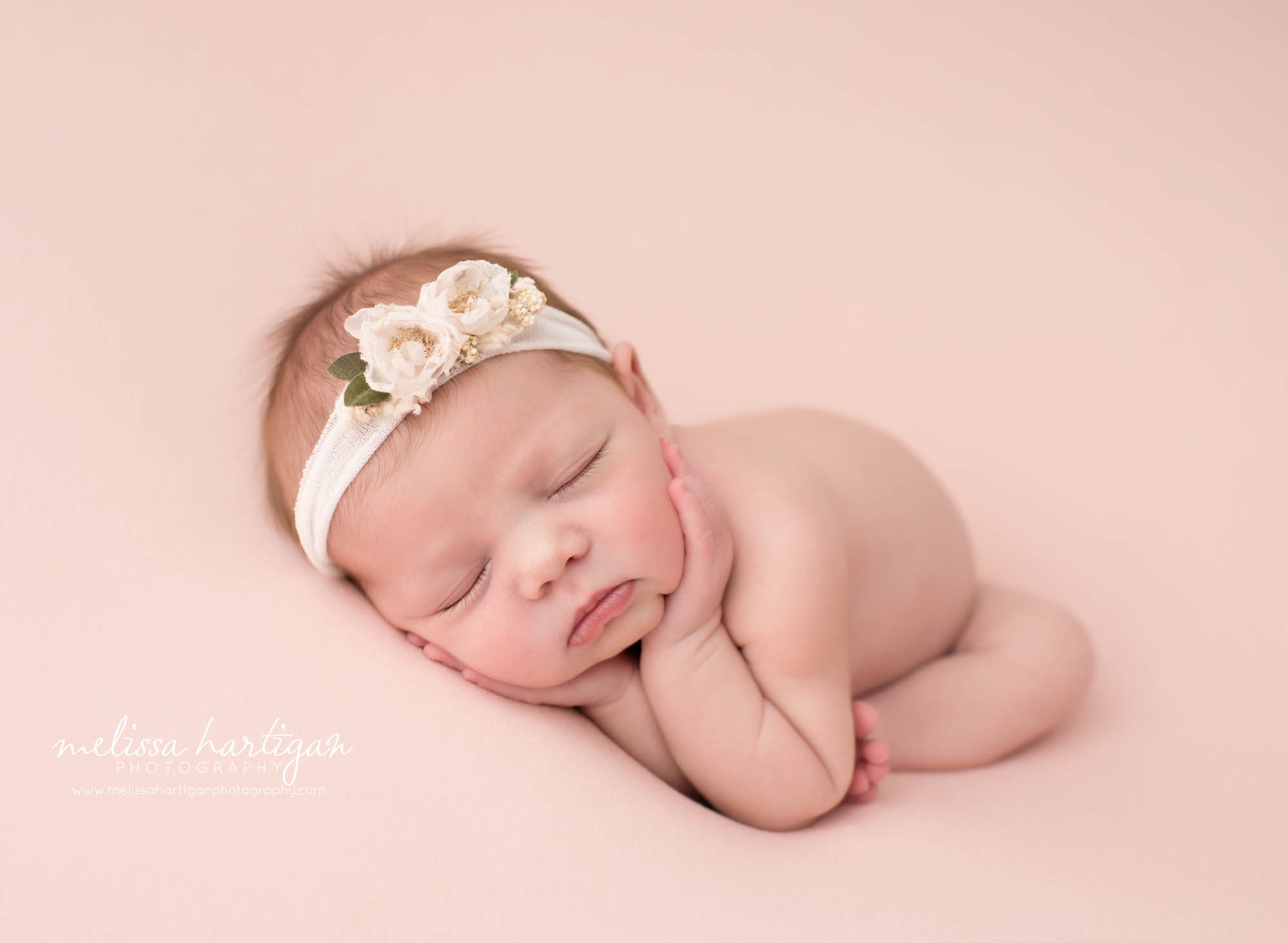 Newborn baby girl posed on pink backdrop wearing flower headband