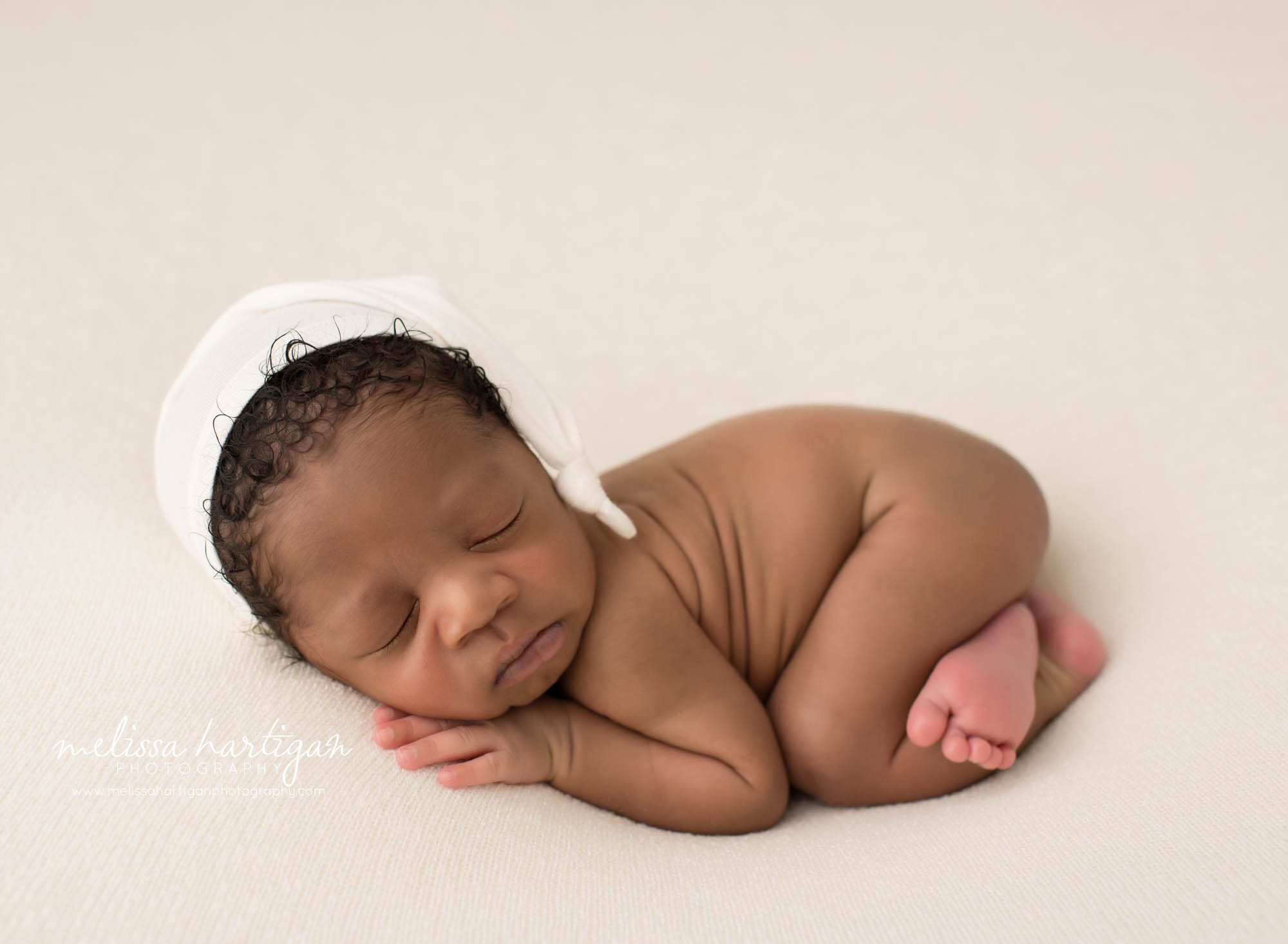 Newborn baby boy posed on tummy wearing white sleepy cap Newborn Photography Durham CT