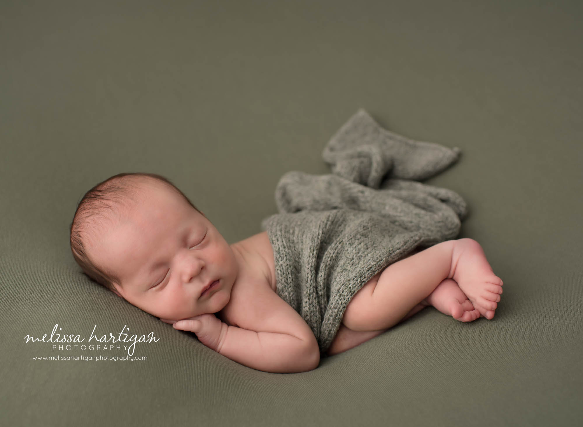 Newborn baby boy posed on side with nit layer draped over him