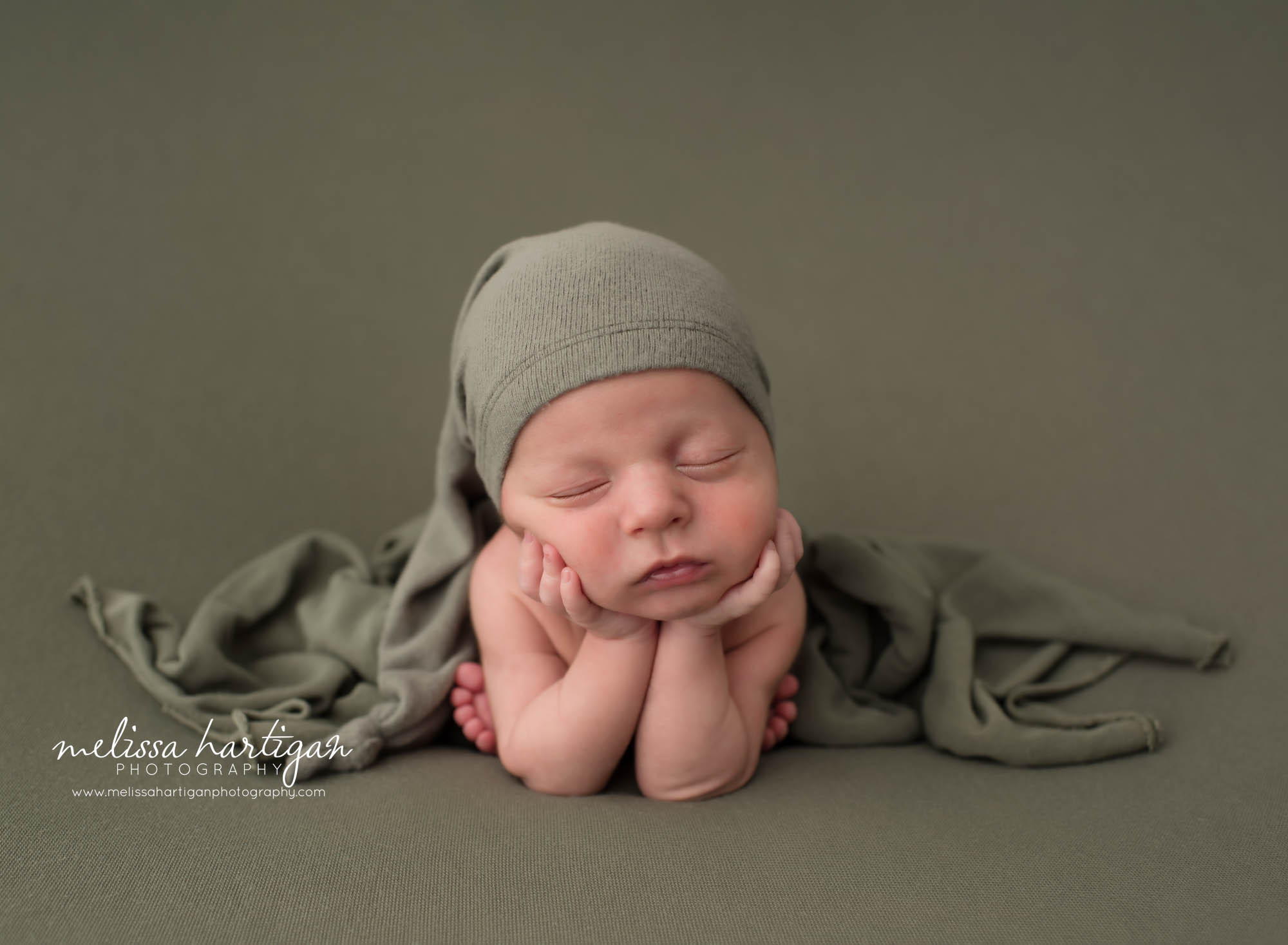 Newborn baby boy posed froggy pose on green backdrop wearing green sleep cap Collinsville CT Newborn Photography