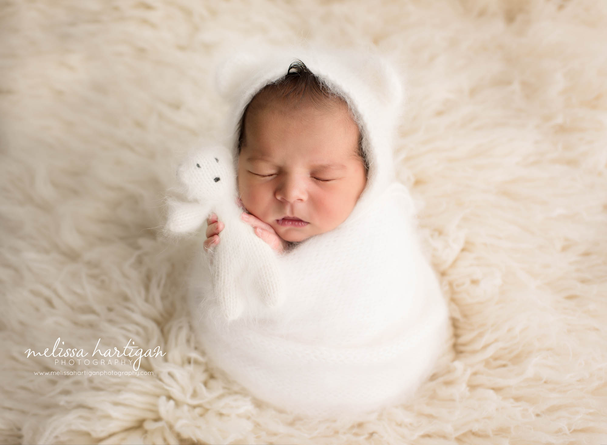 Newborn baby boy posed with knitted white teddy tear wearing matching teddy bear bonnet wrapped in knitted white wrap Newborn Photography Norwich CT