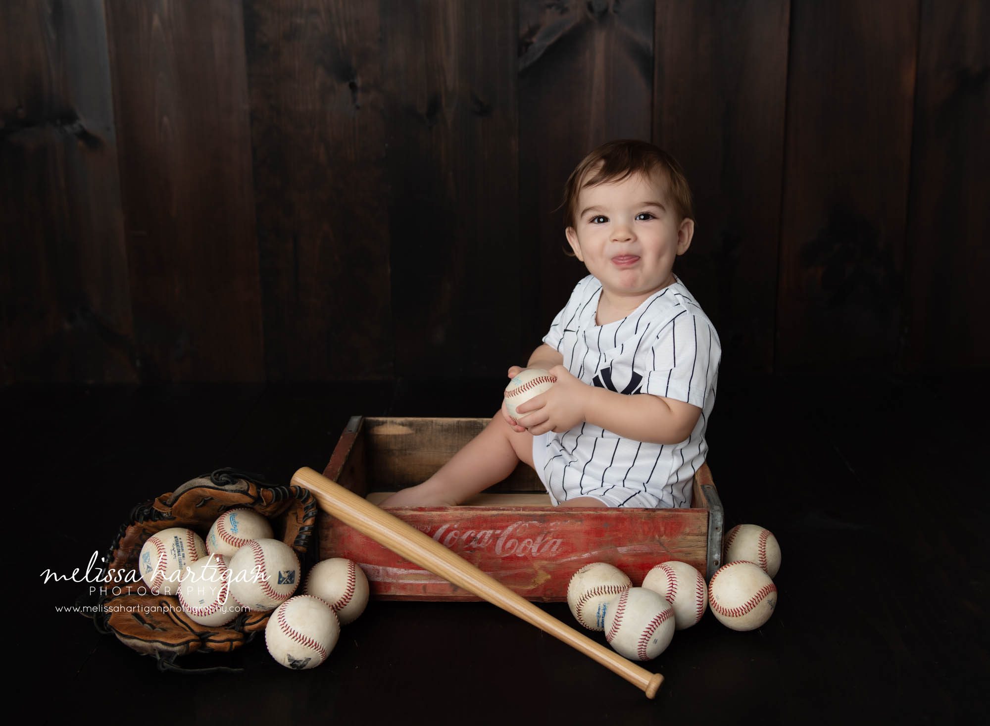 Baby boy happy smiling holding baseball sitting in wooden crate NY yankees themed setup