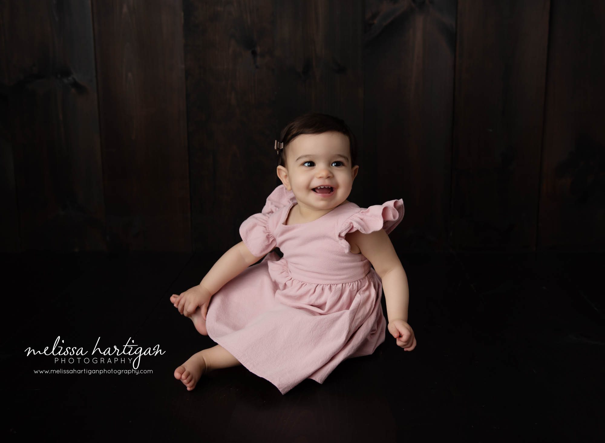 Baby girl happy smiling holding foot sitting on wooden boards in photostudio