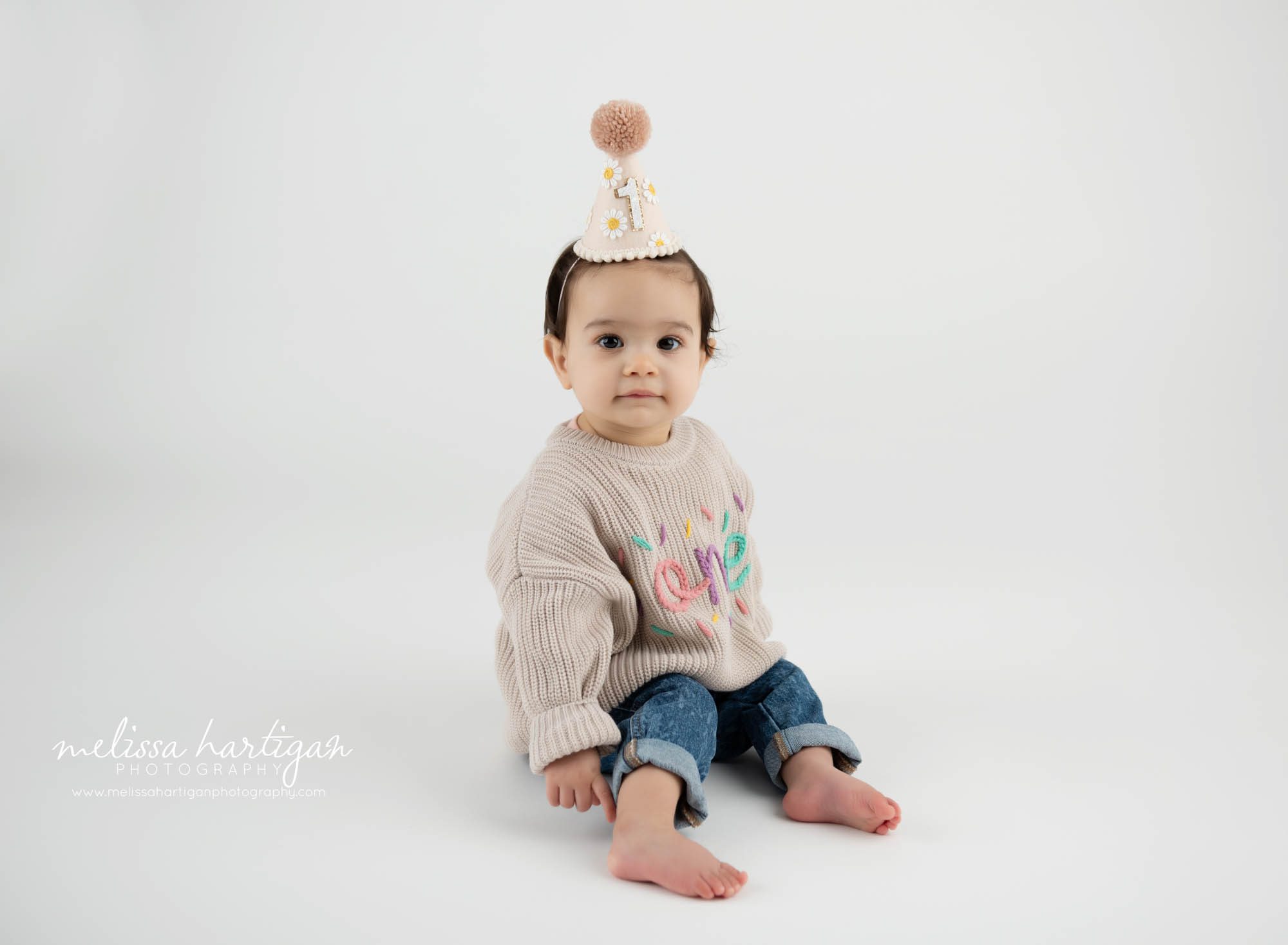 Baby girl sitting wearing birthday hat and ONE on sweater