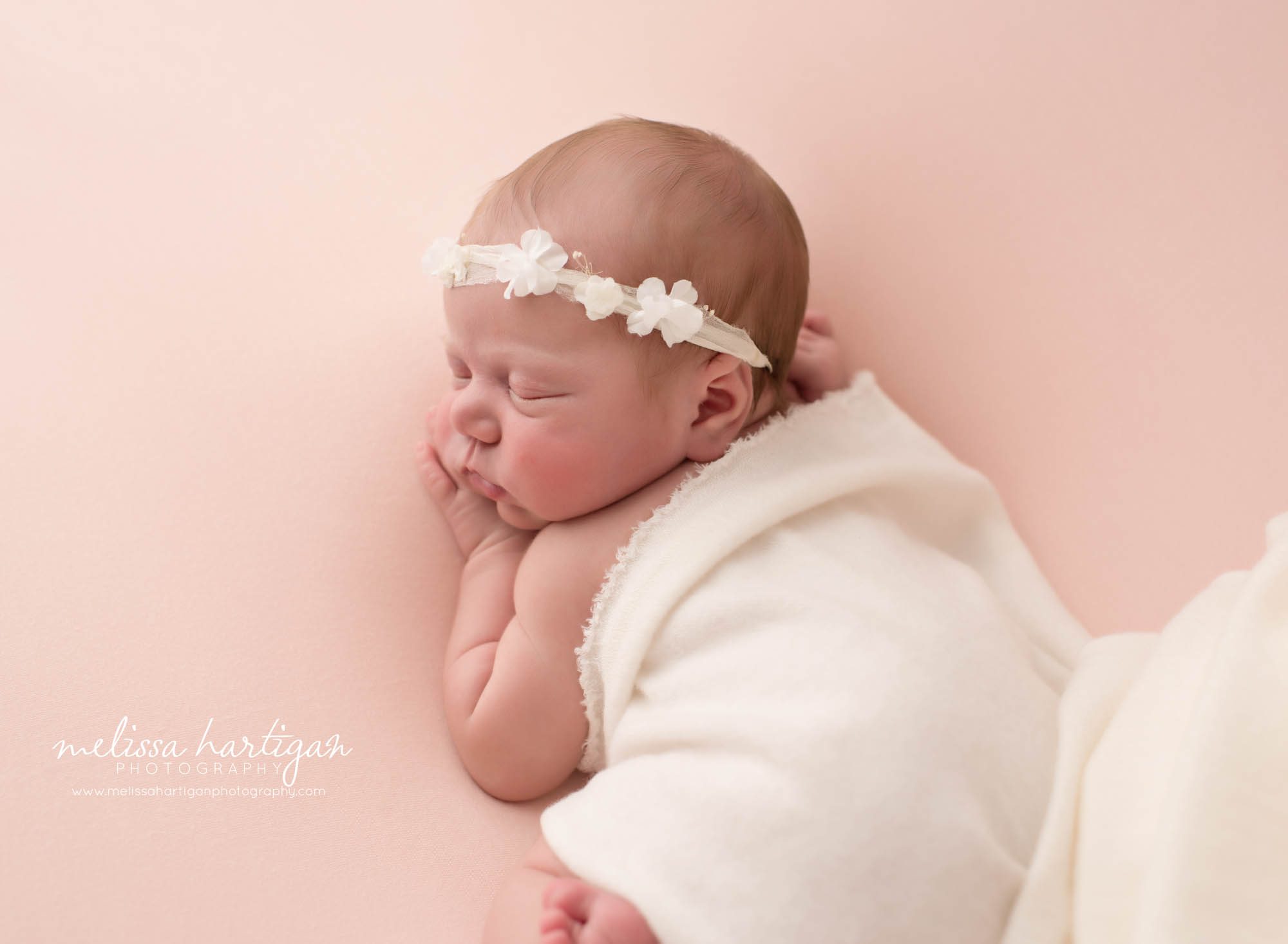 Newborn baby girl posed on tummy with white layer draped over her back