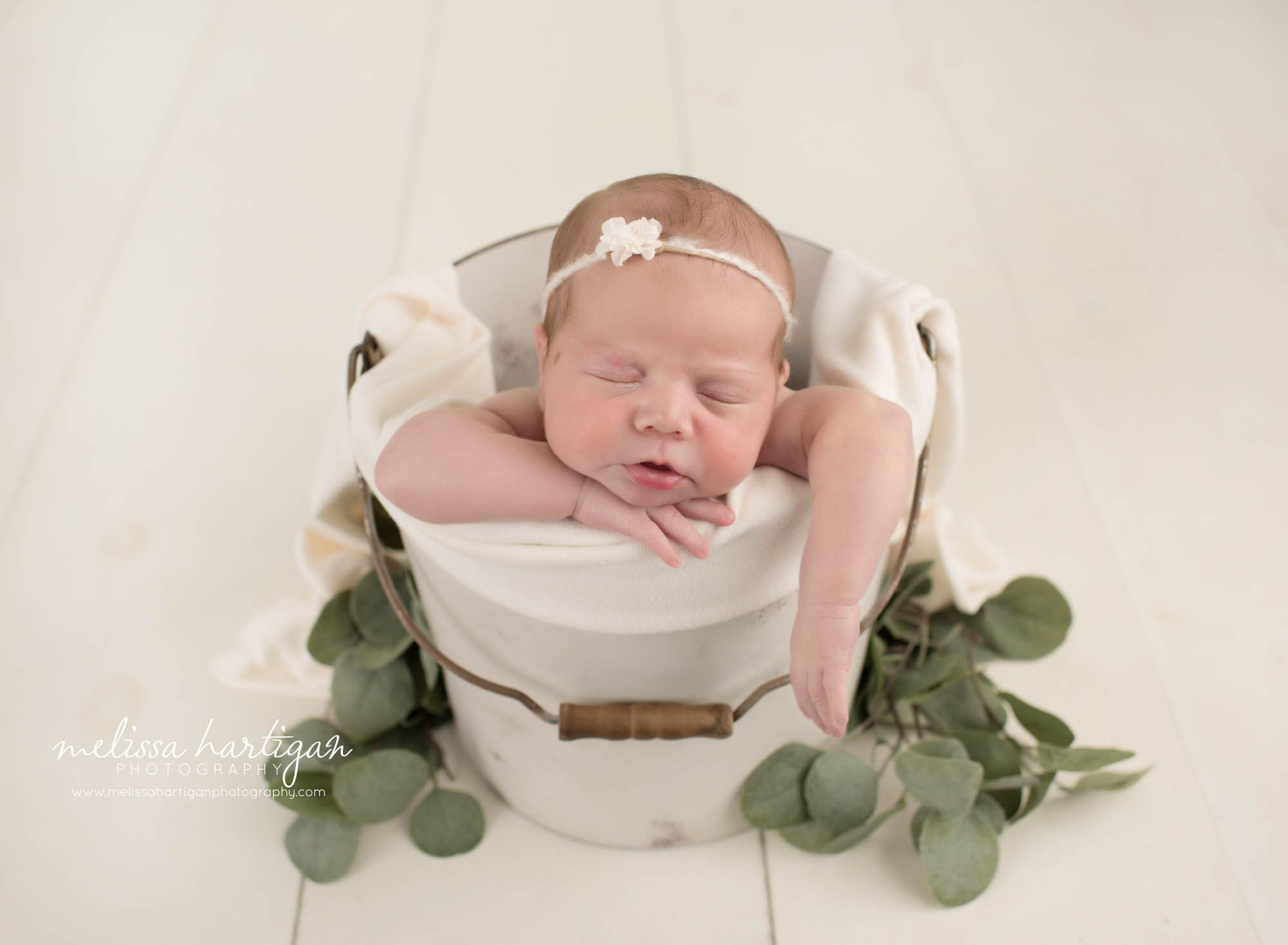 Newborn baby girl posed in bucket wearing headband
