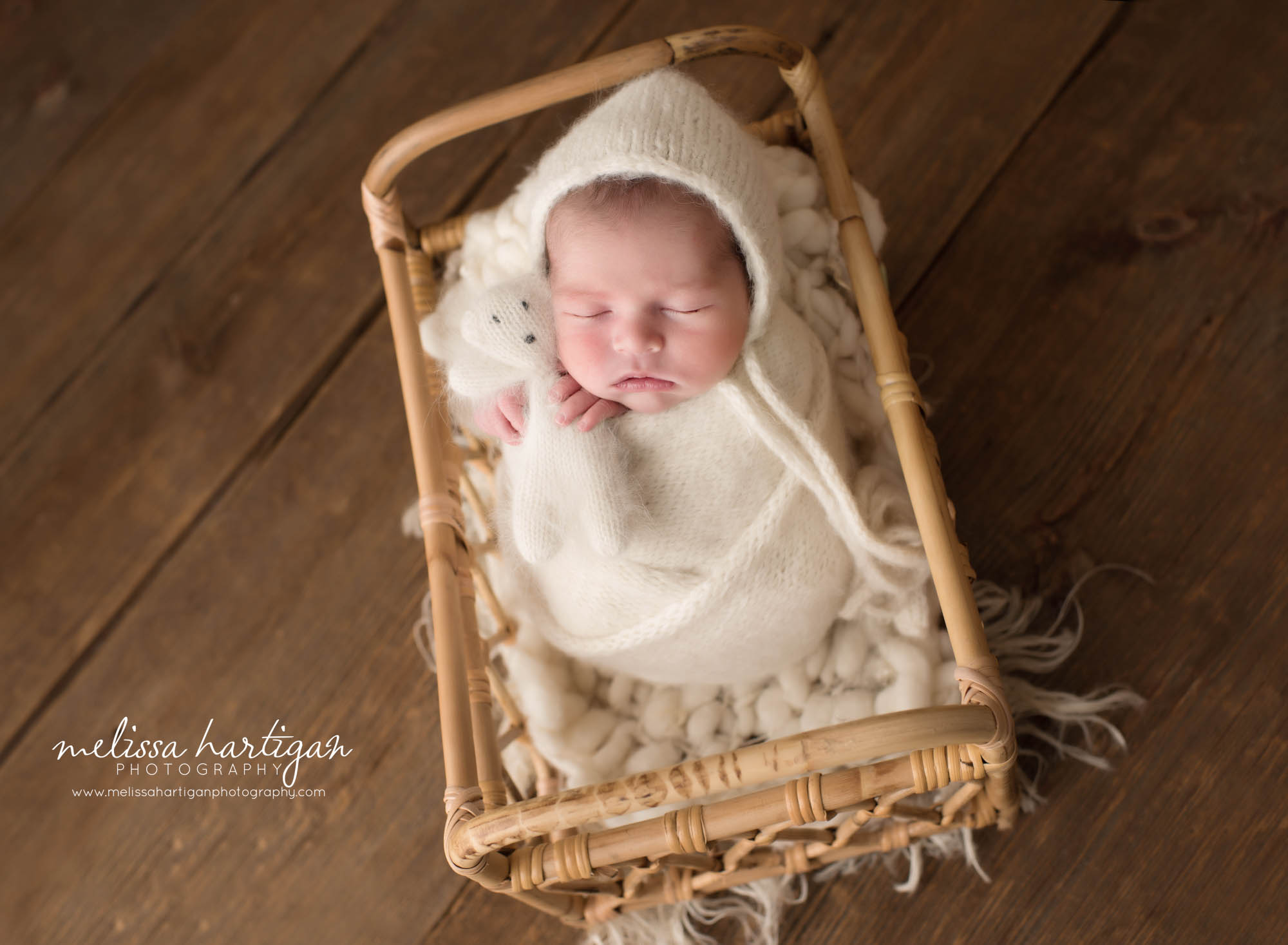 Newborn baby boy posed in basket swaddled in cream knit wrap and bonnet holding a knitted teddy bear Newborn Photography Hebron CT