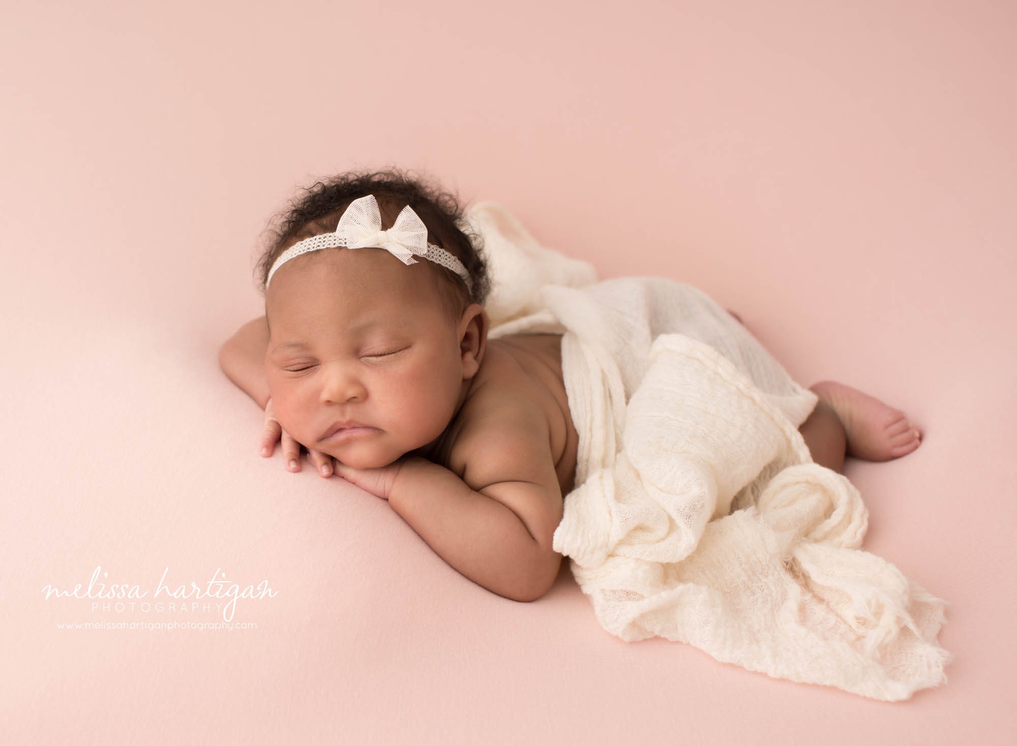 Newborn baby girl posed on tummy with hands under cheek