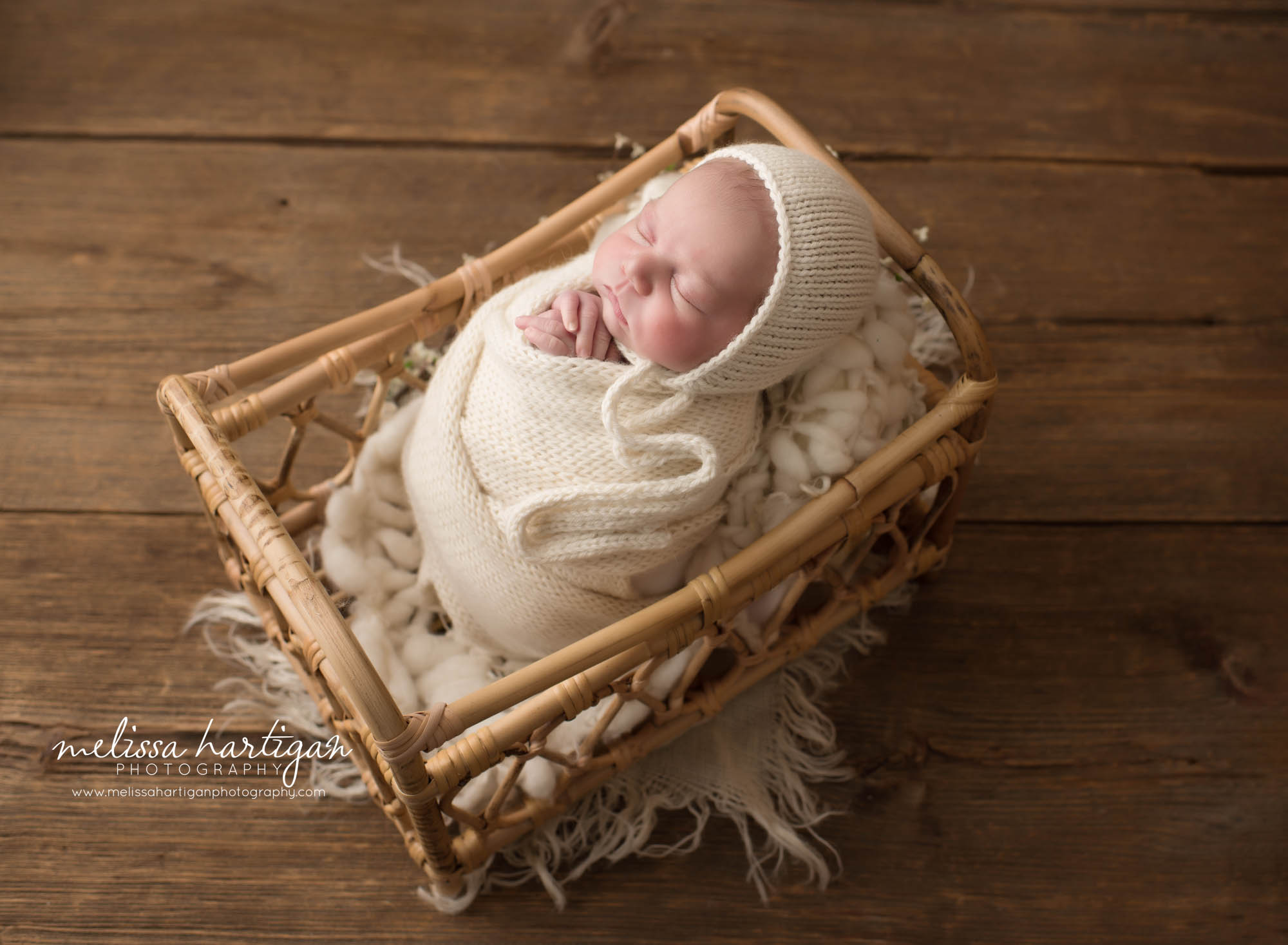 Newborn baby girl posed in basket swaddled in cream knitted layer wrap