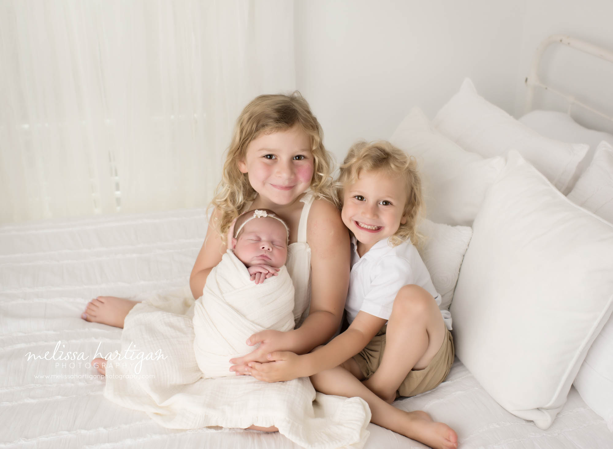 Newborn baby sister posed with big sister and big brother sitting on bed for siblings pose Newborn Photography Ivoryton CT