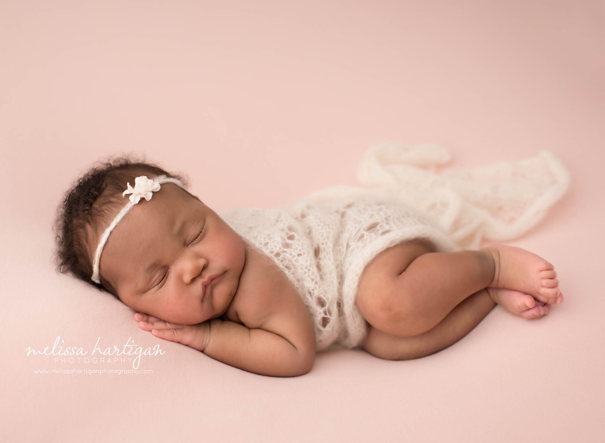 Newborn baby girl posed on side wearing headband and knit lace draped over