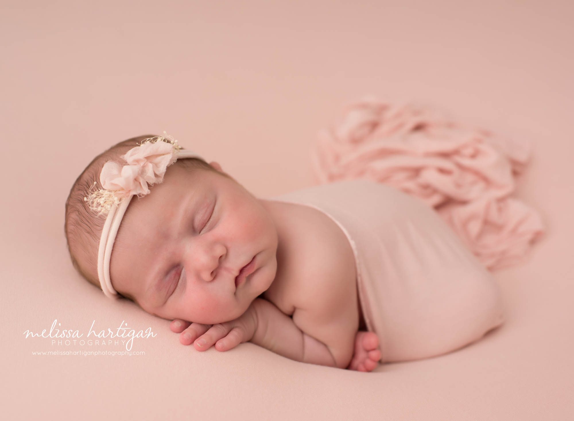 Newborn baby girl posed with hand under cheek on pink backdrop with pink bow headband