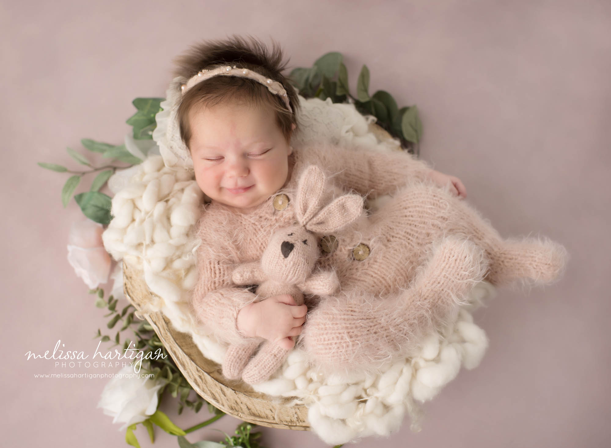 Newborn baby girl posed in wooden bowl with knitted bunny