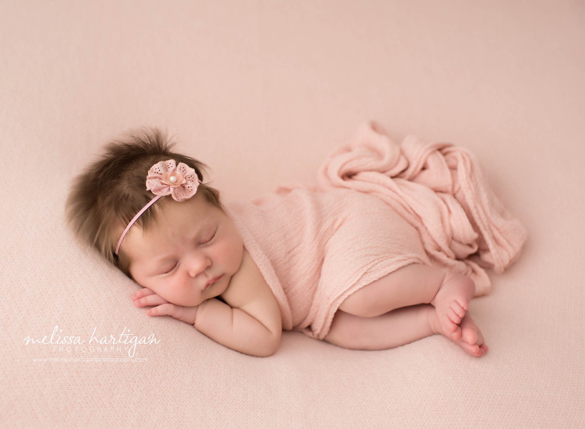 Newborn baby girl posed on pink backdrop on side wearing flower headband Hebron CT Newborn Photography