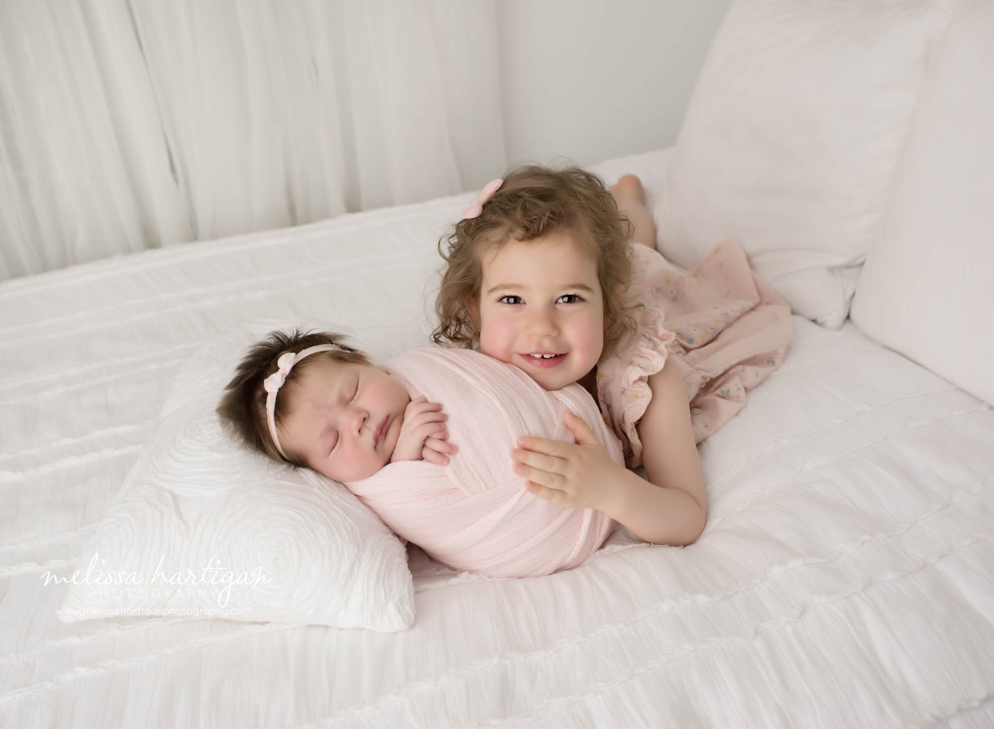 Big sister cuddling with newborn baby sister in sibling pose