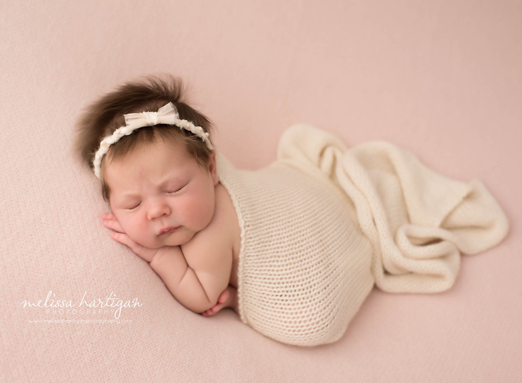 Newborn baby girl posed on tummy with hand under cheek with cream knitted layer draped over