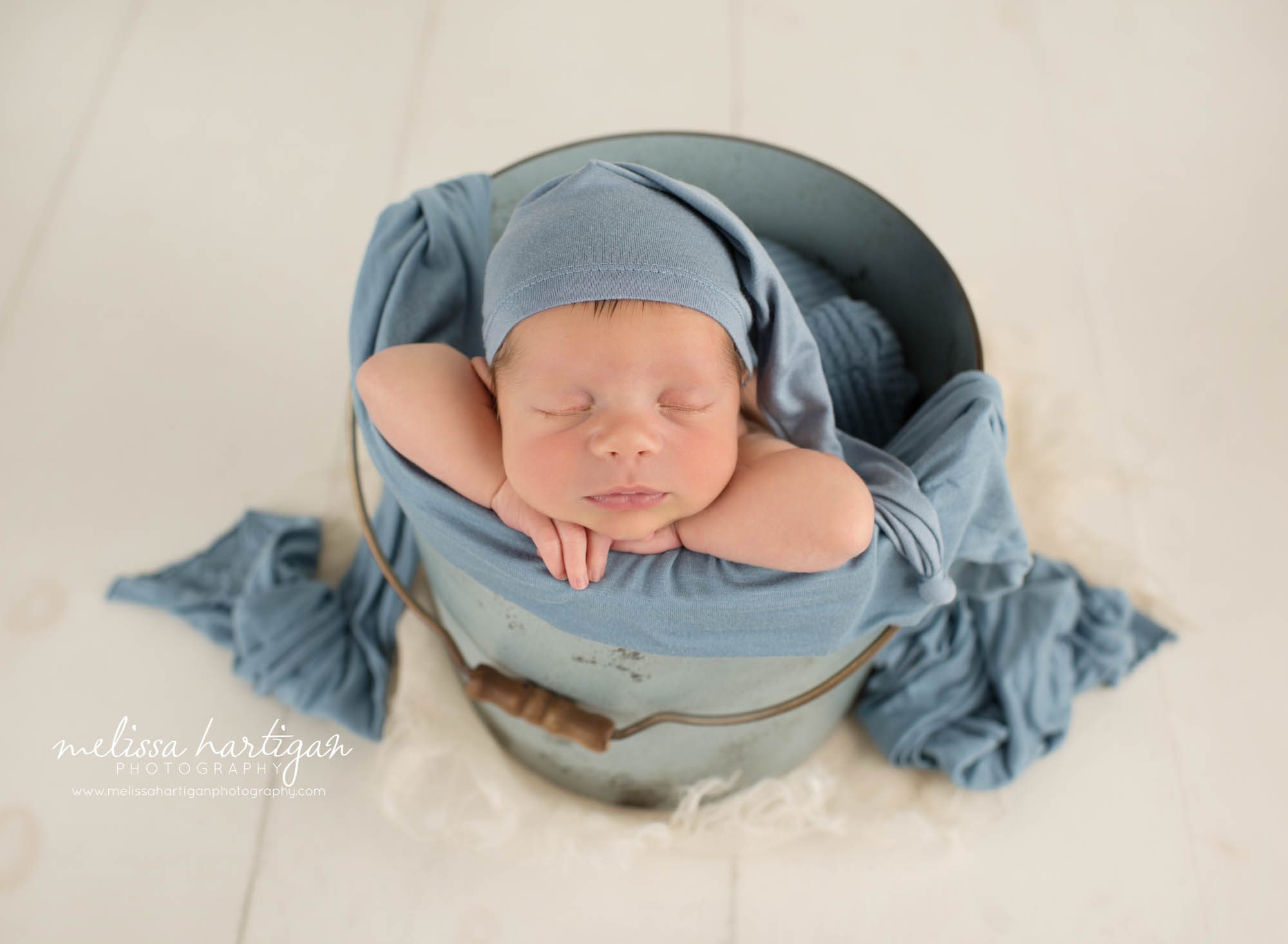 Newborn baby boy posed in bucket wearing blue sleepy cap