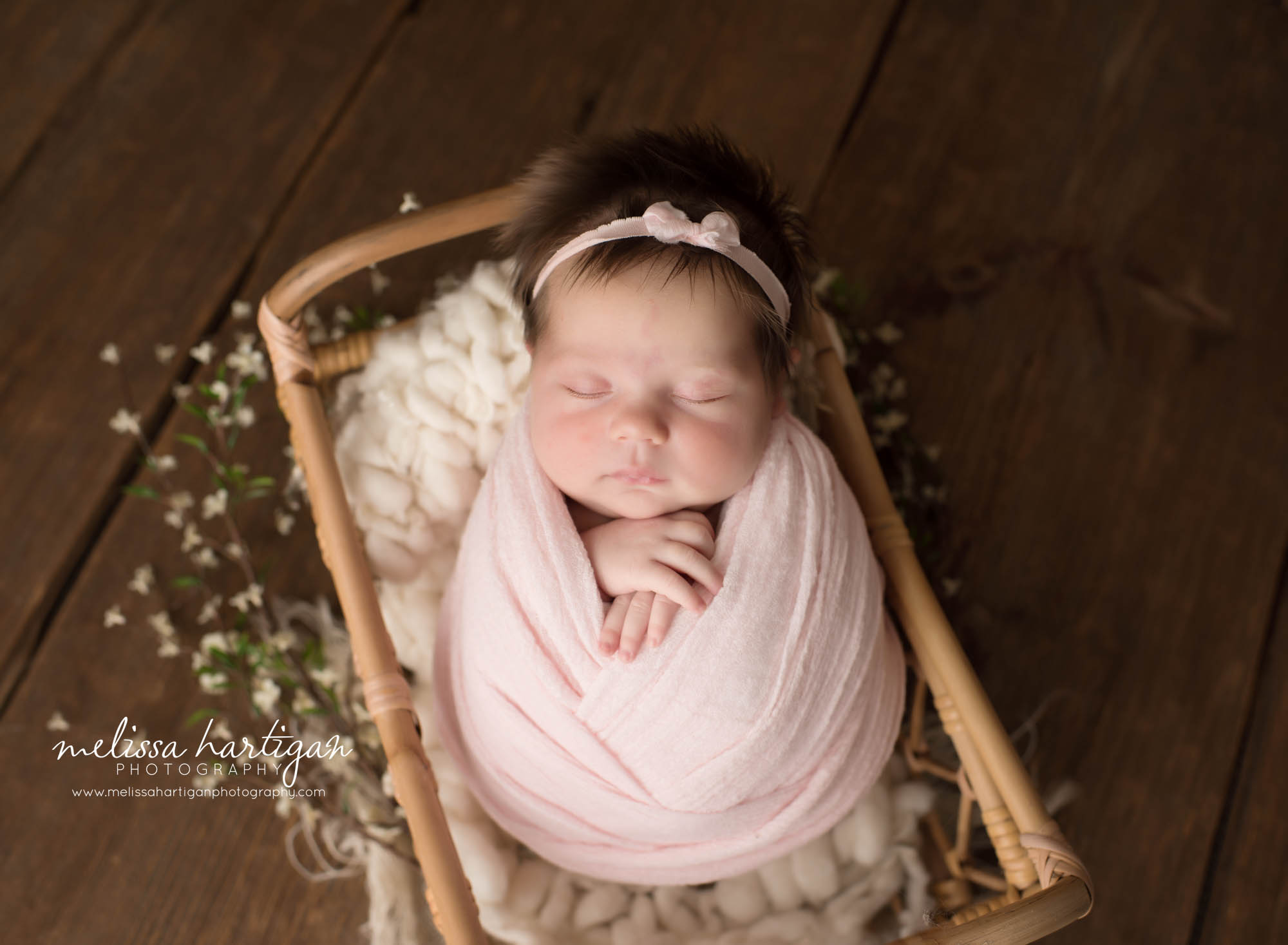 Newborn baby girl posed in basket swaddled in pink wrap