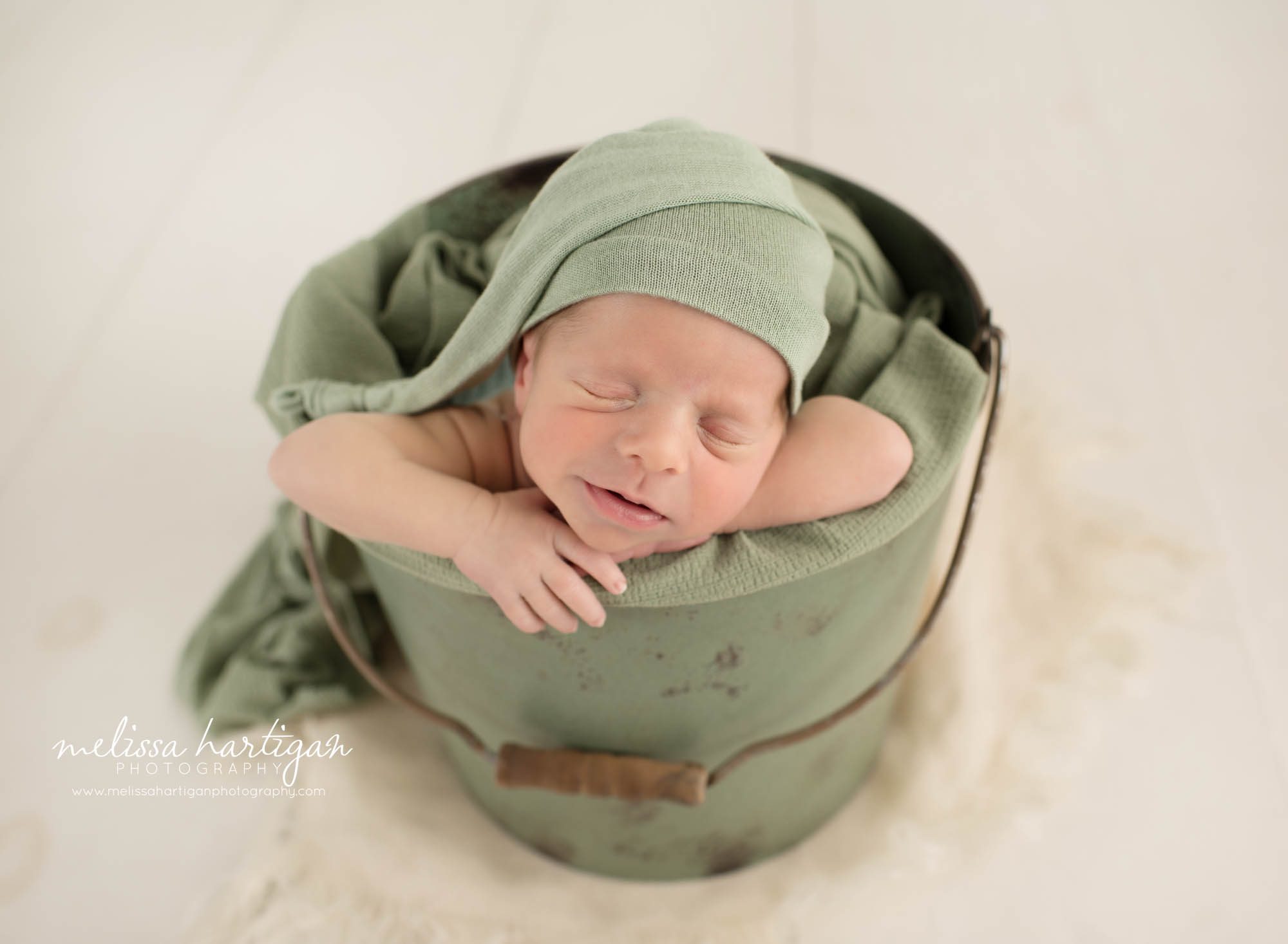Newborn baby boy posed in bucket wearing green sleepy cap Colchester CT Newborn Photography