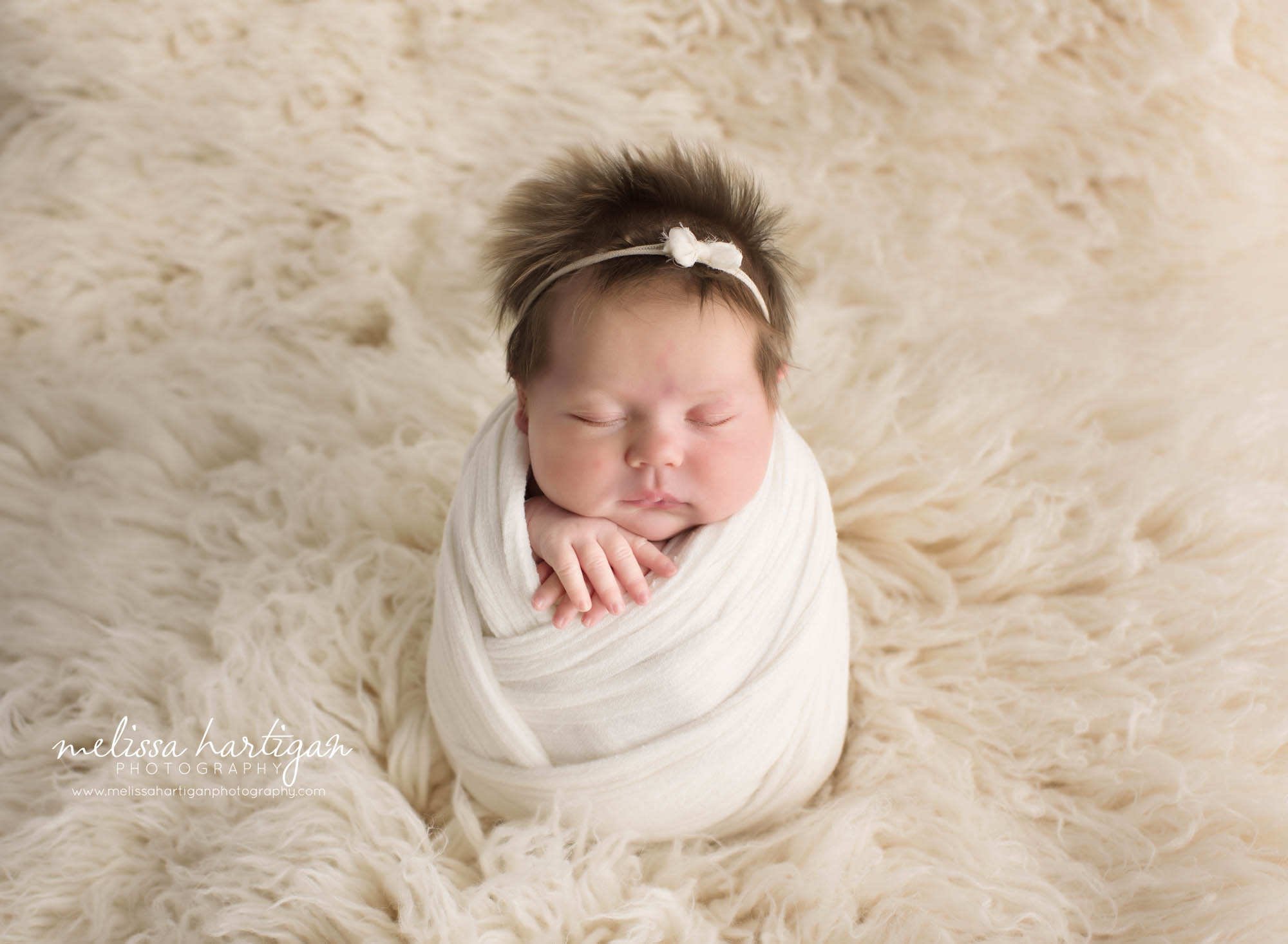Newborn baby girl posed on cream flokati rug swaddled in cream white wrap