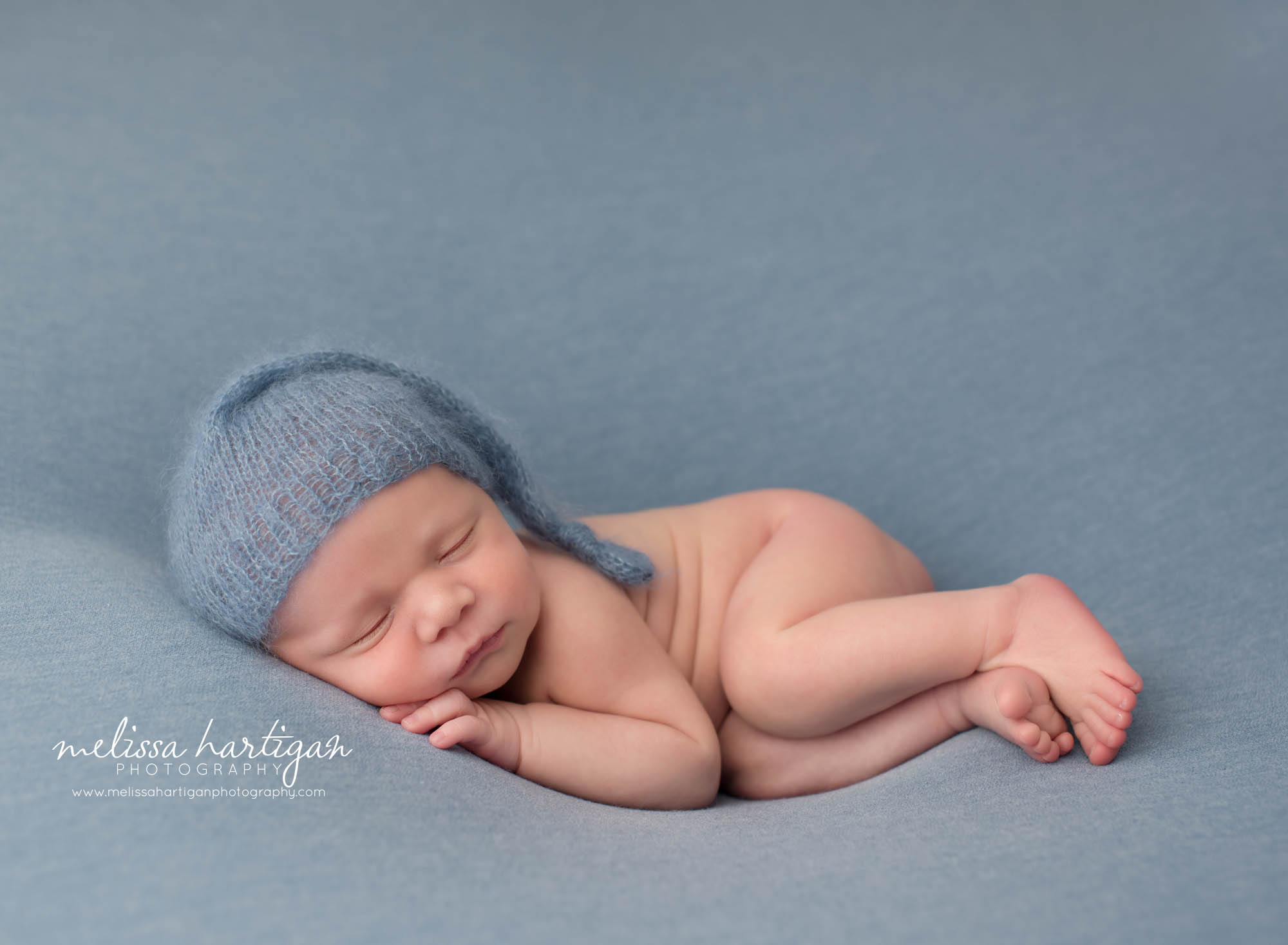 Newborn baby boy posed on blue backdrop blue sleepy cap Newborn Photography Charlton MA