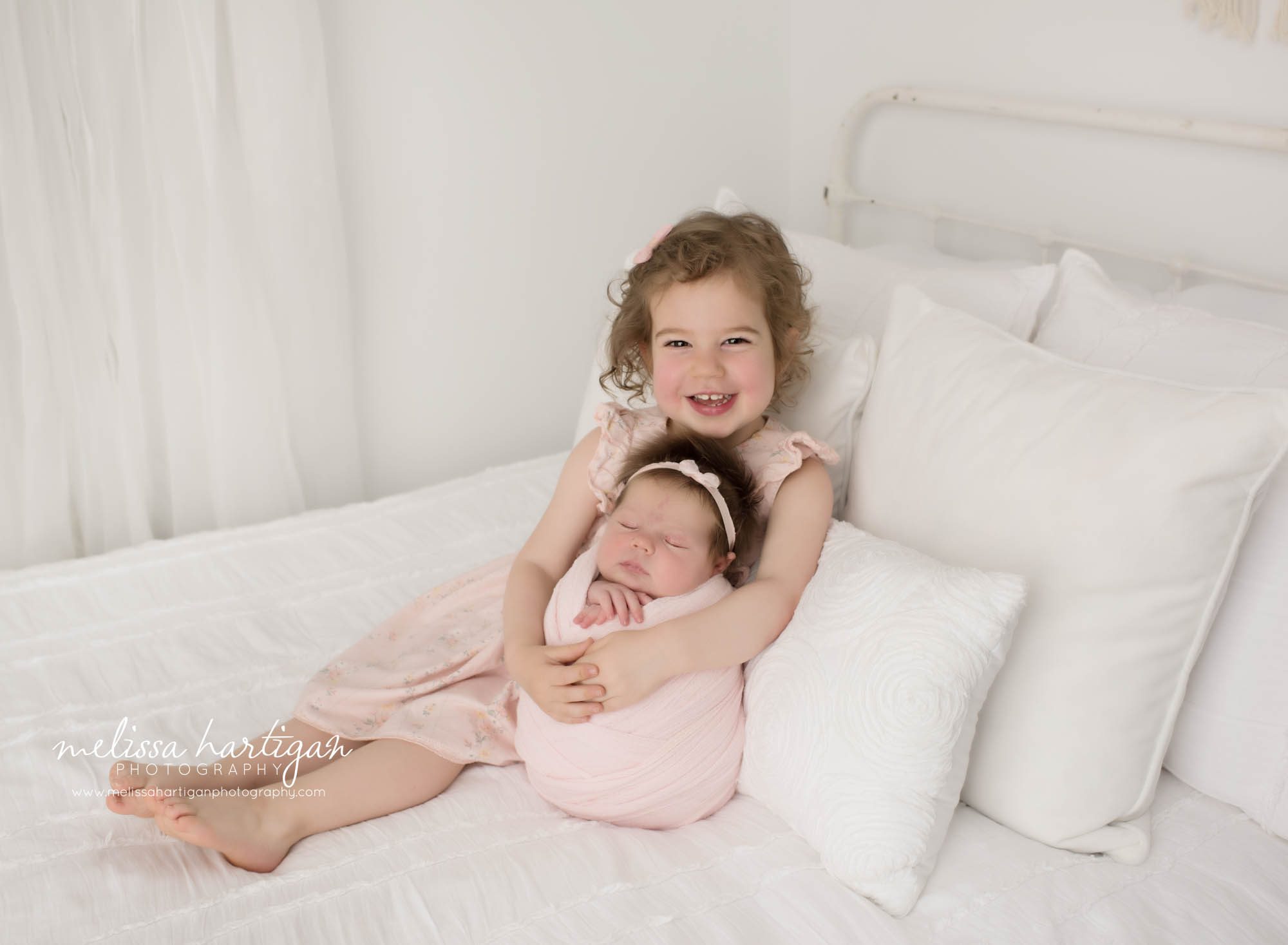 Big sister cuddling newborn sister on bed in studio for newborn photoshoot Hebron CT Newborn Photography