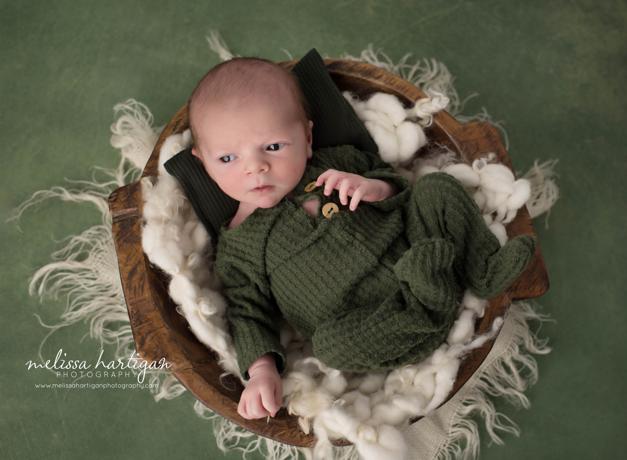Newborn baby boy wearing green knit waffle outfit posed in wooden bowl