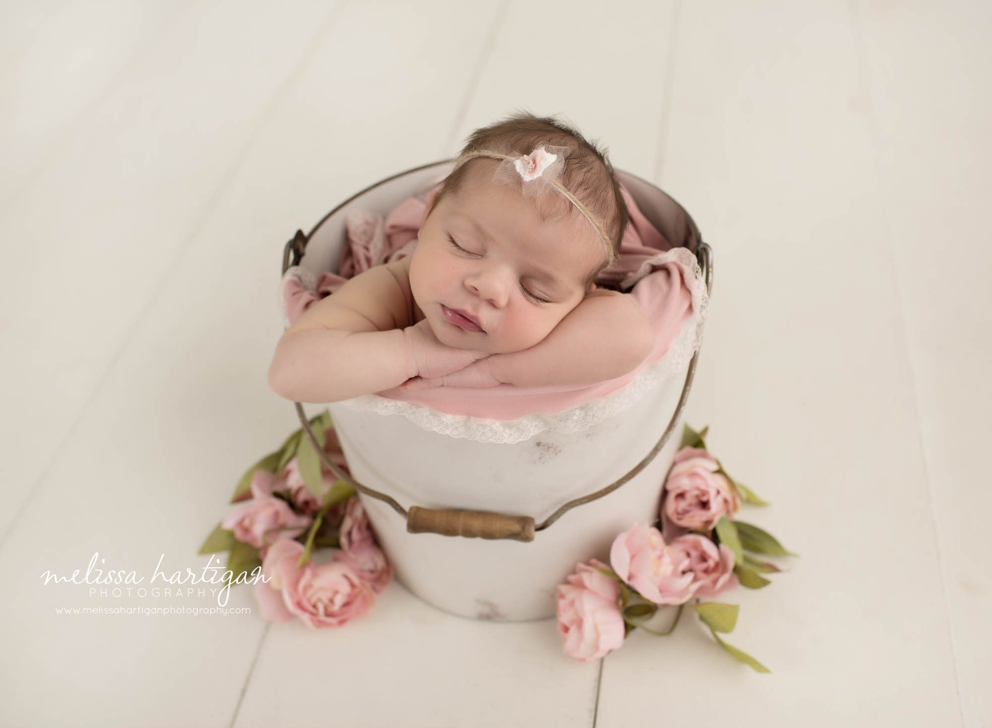 Newborn baby girl posed in bucket sleeping with flowers