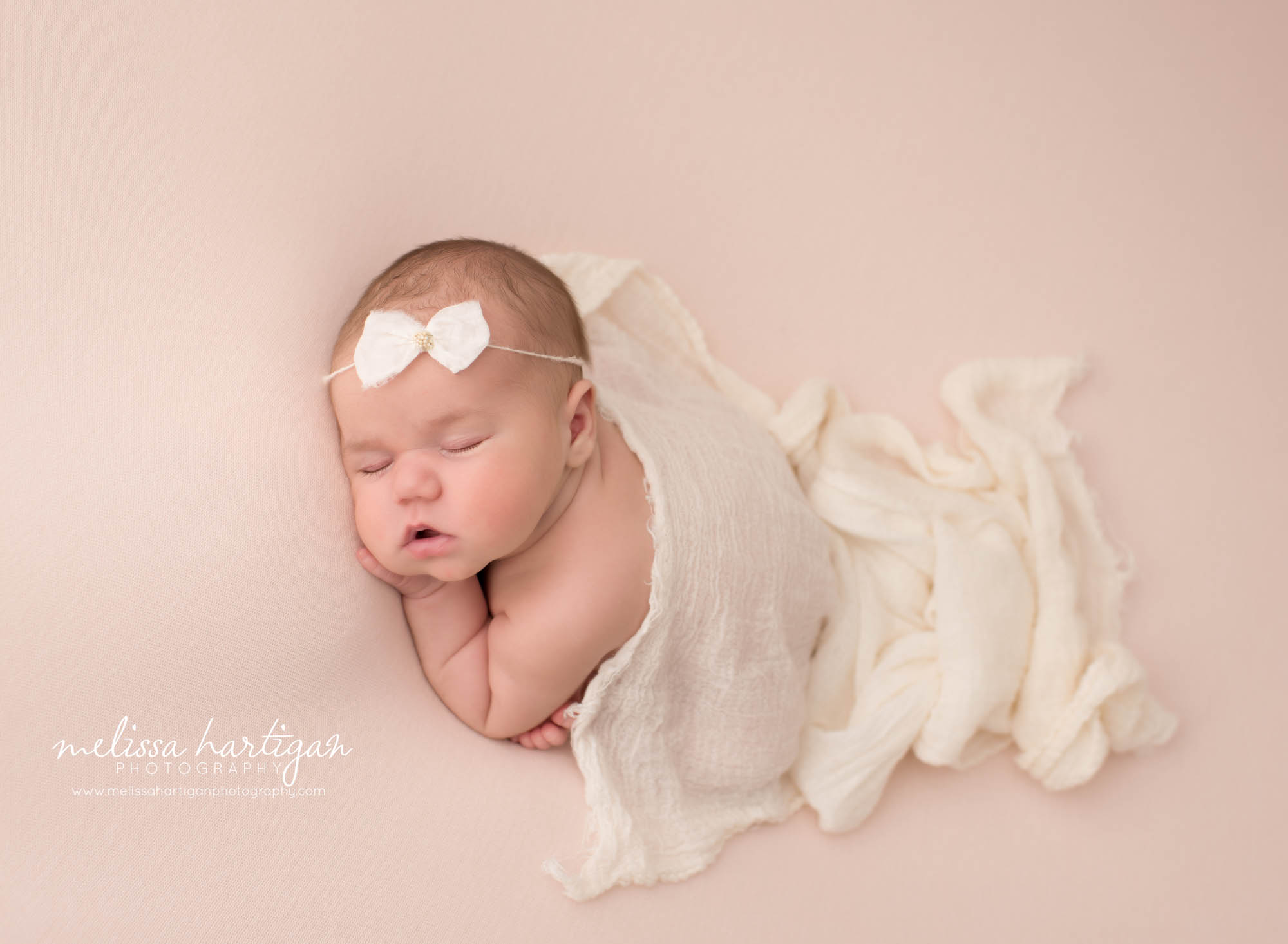 Newborn baby girl posed on tummy with cream layer draped over her Newborn Photography Ludlow MA