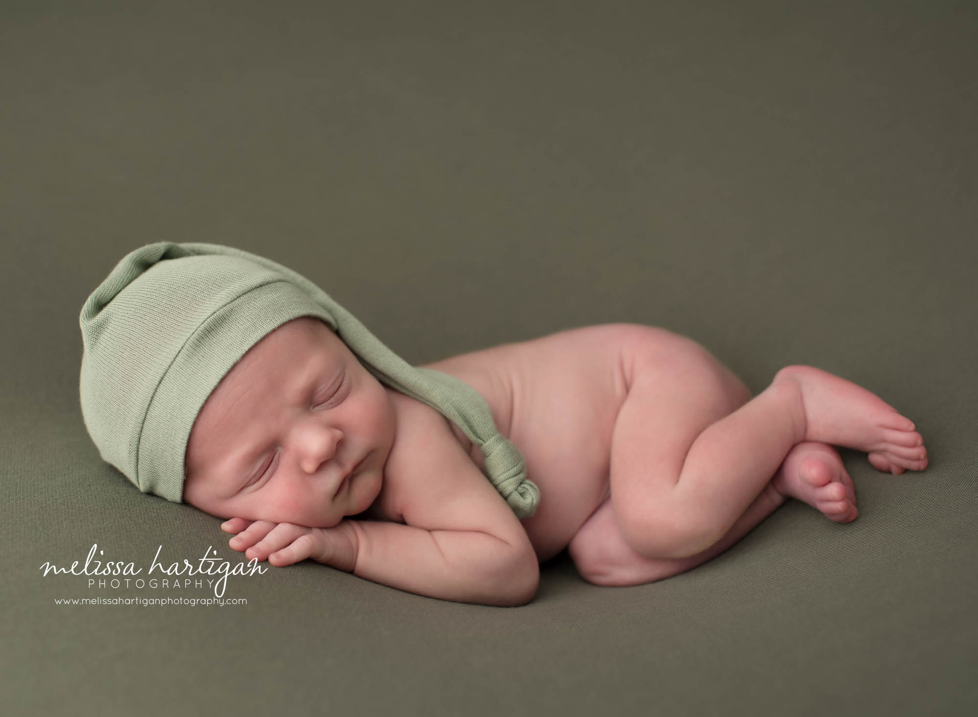 Newborn baby boy posed on side wearing green sleepy cap
