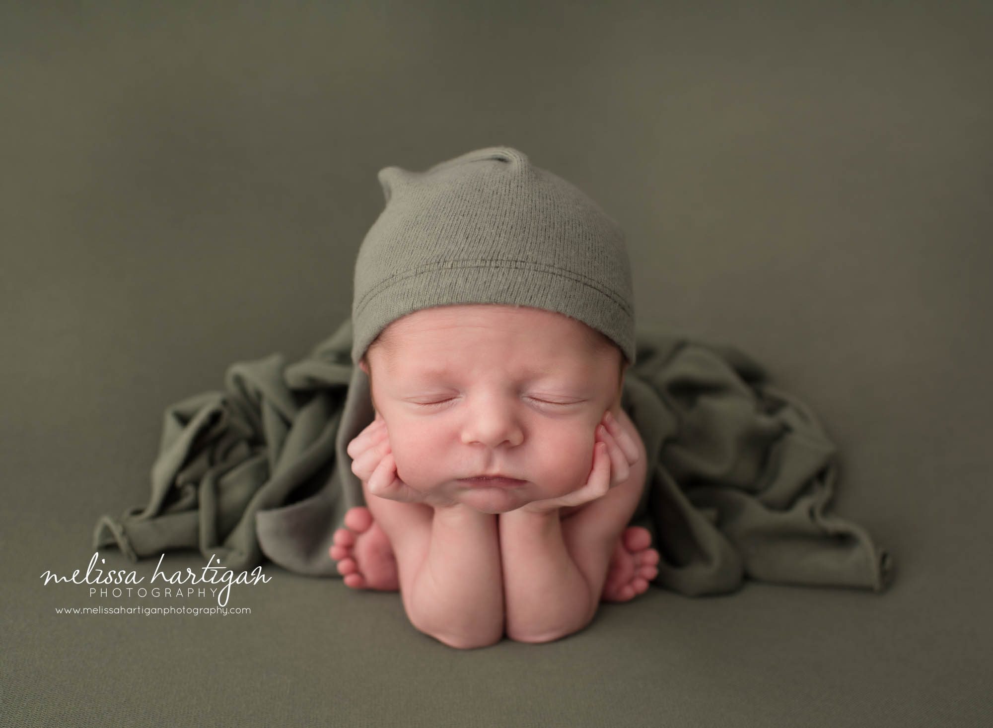 Newborn baby boy posed froggy pose wearing green sleepy cap