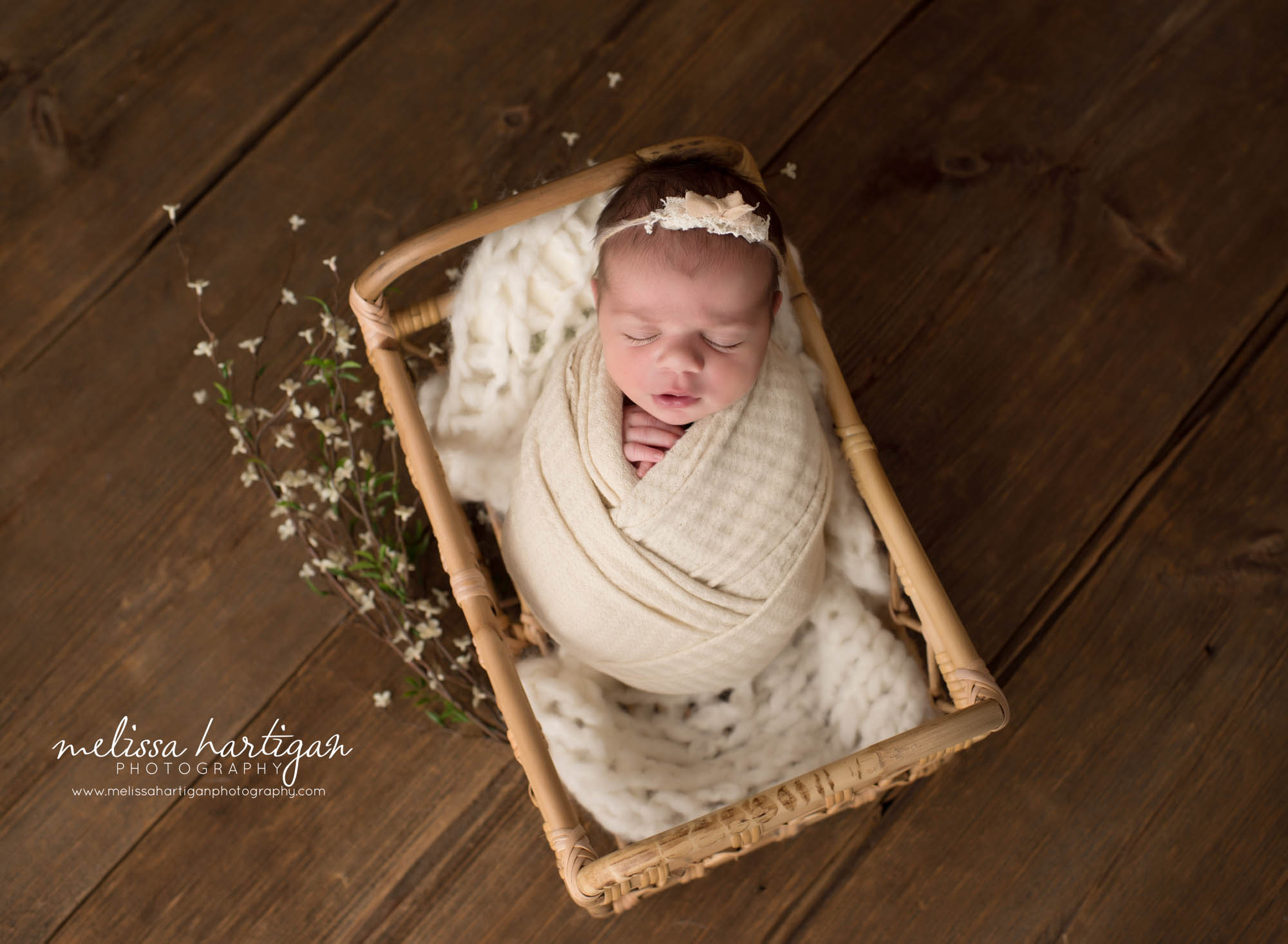 Newborn baby girl posed in basket wrapped in cream wrap